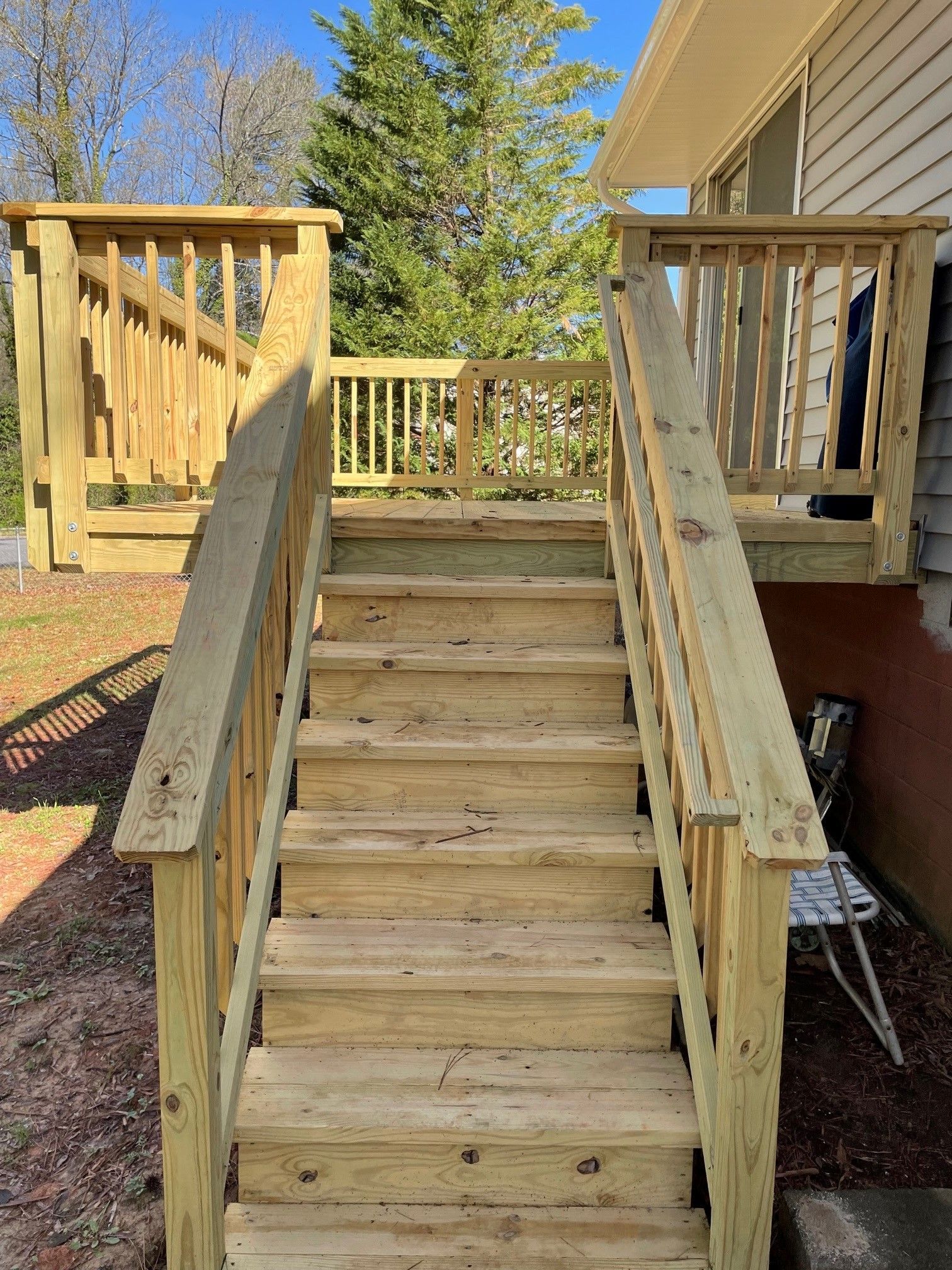 Wooden outdoor staircase with handrails leading up to a porch beside a house