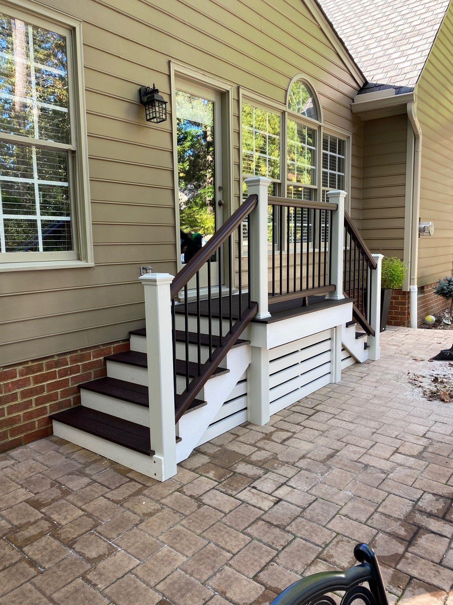 Front porch entrance with short stairs, white railings, and a small ramp beside tan house siding