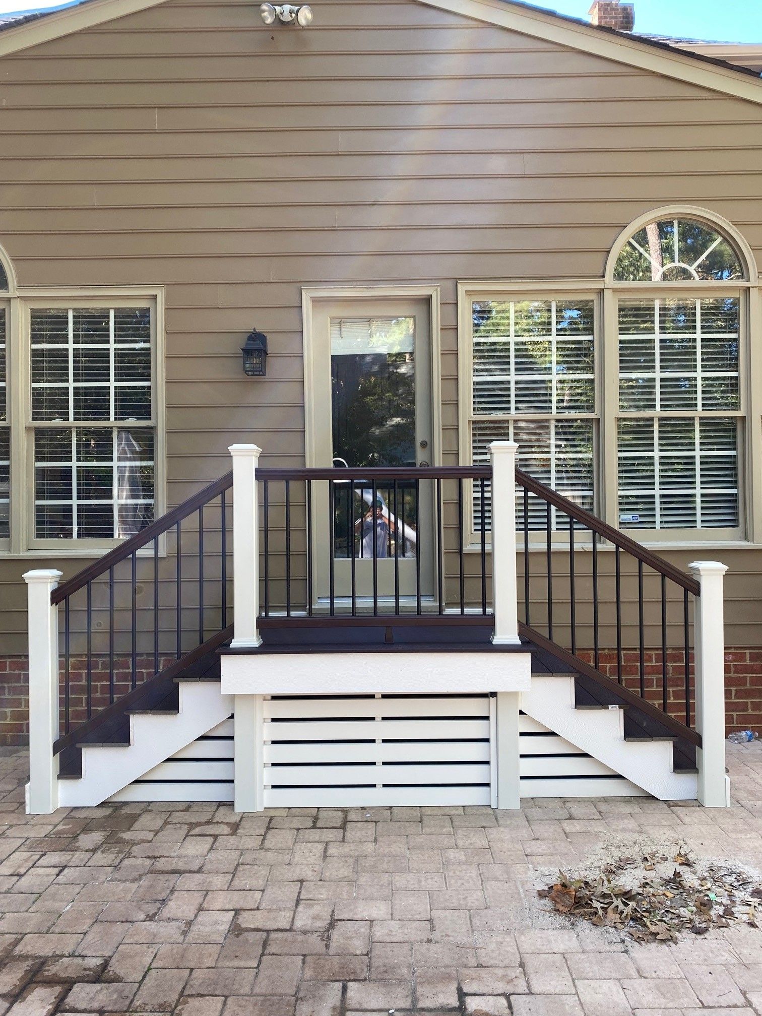 Front porch with white railings, steps, large windows, and brick paver patio on a beige house