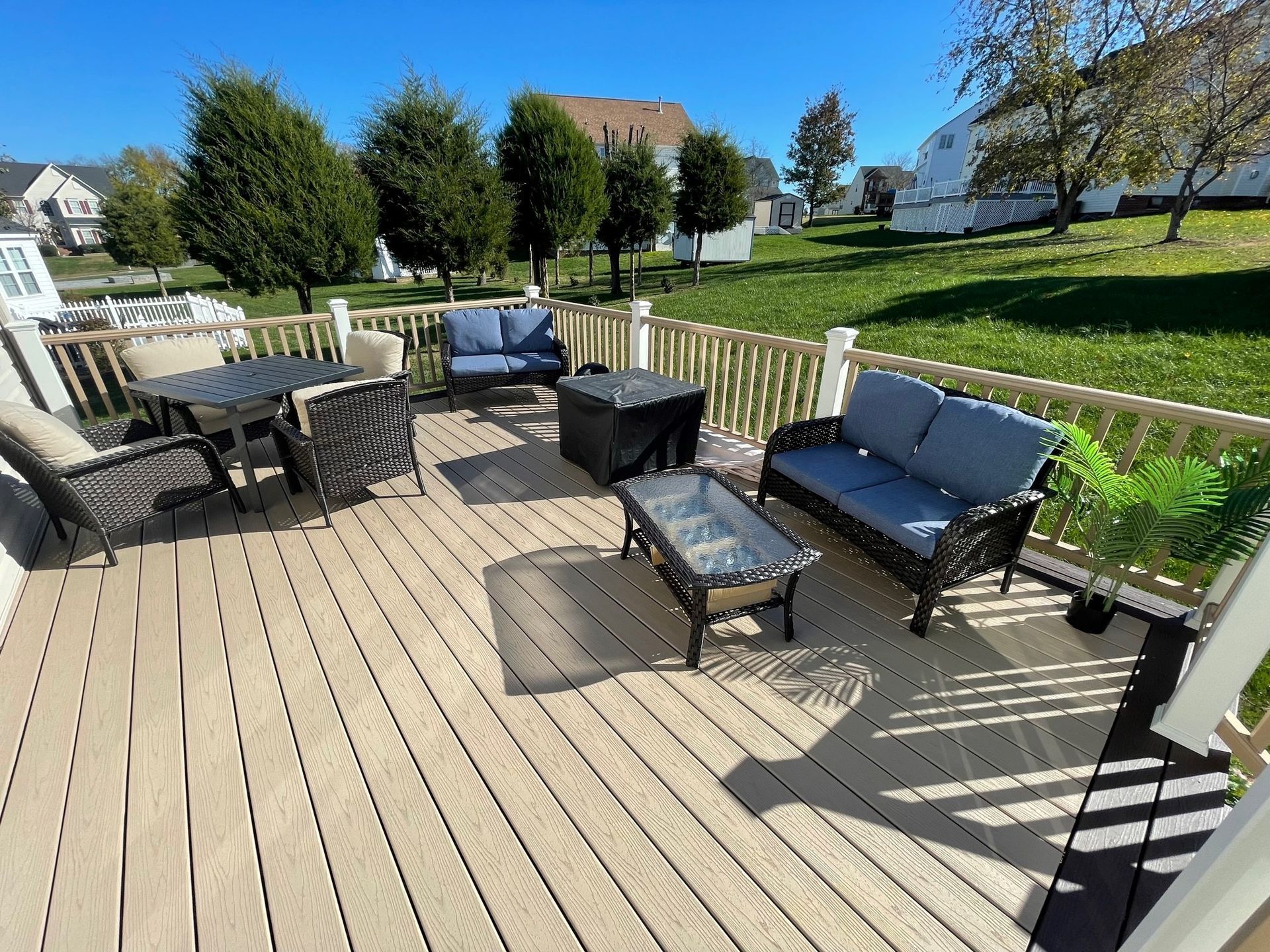 Sunny backyard deck with patio chairs, blue bench, and a glass coffee table overlooking a green lawn