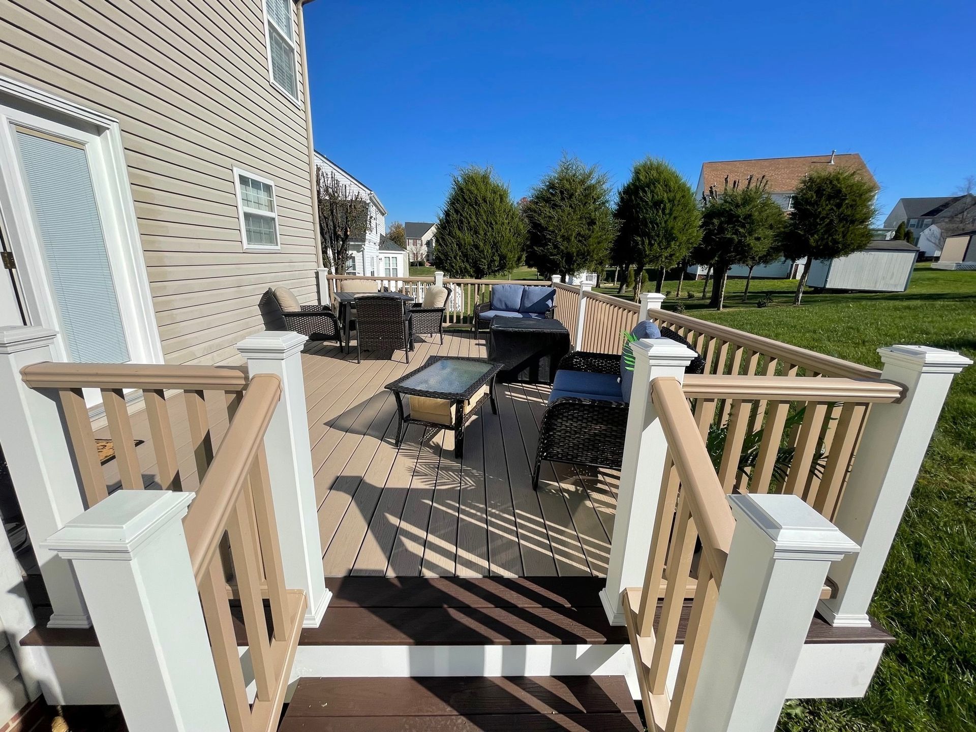 Patio with outdoor seating, white railing, and a brick house under a clear blue sky