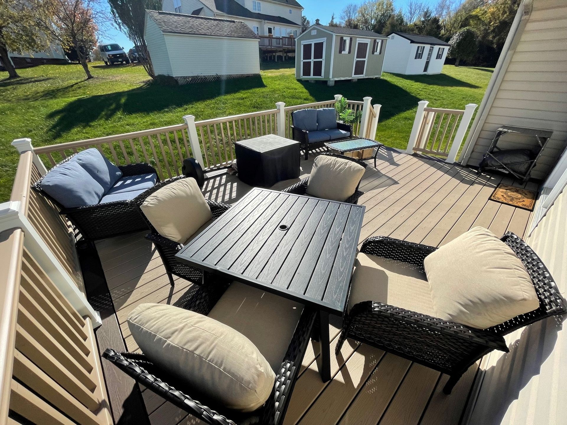 Outdoor patio with black wicker furniture, beige cushions, and a gray table in a sunny backyard