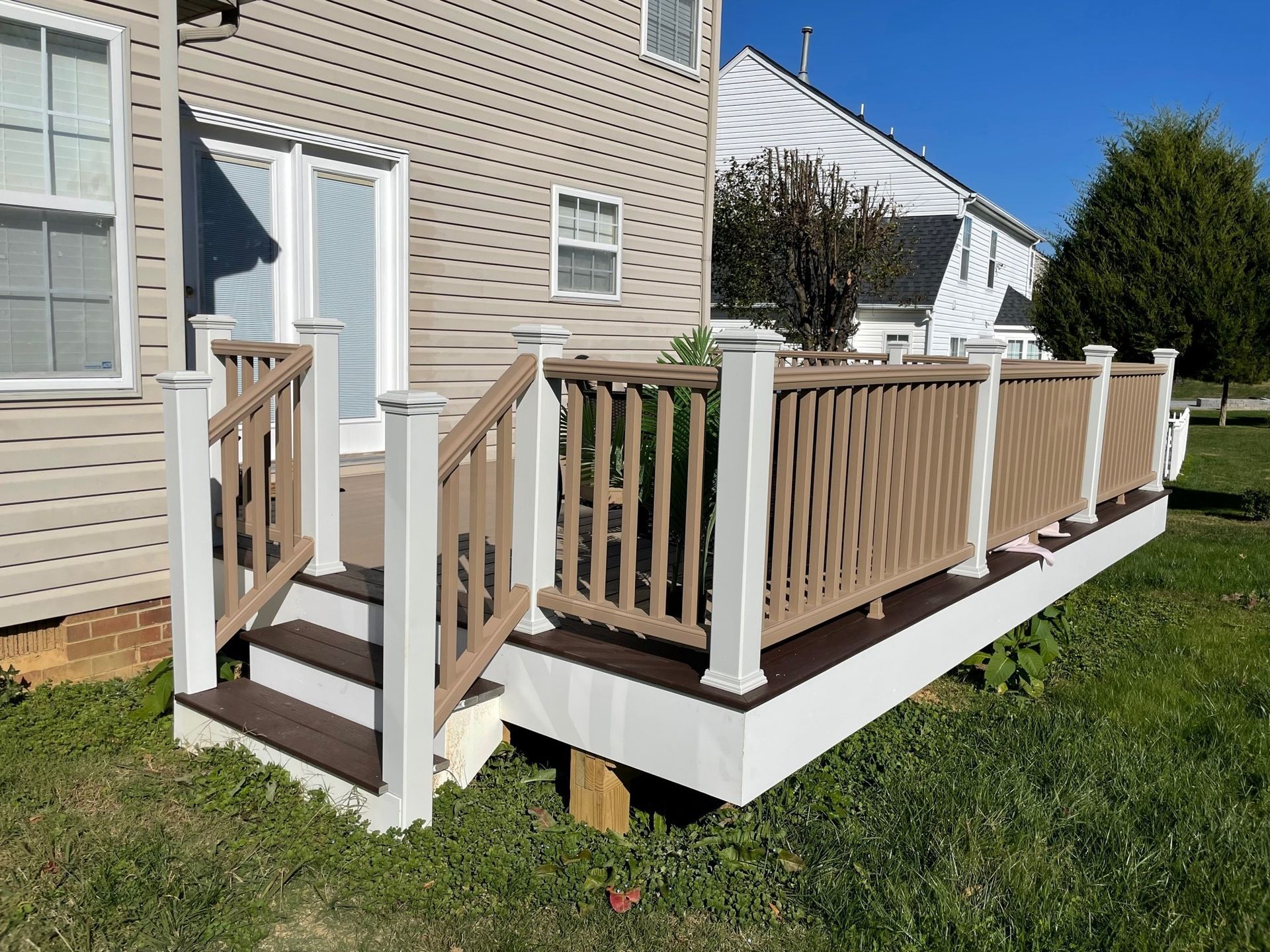 Small wooden wheelchair ramp and porch extension beside a beige house with white railings.