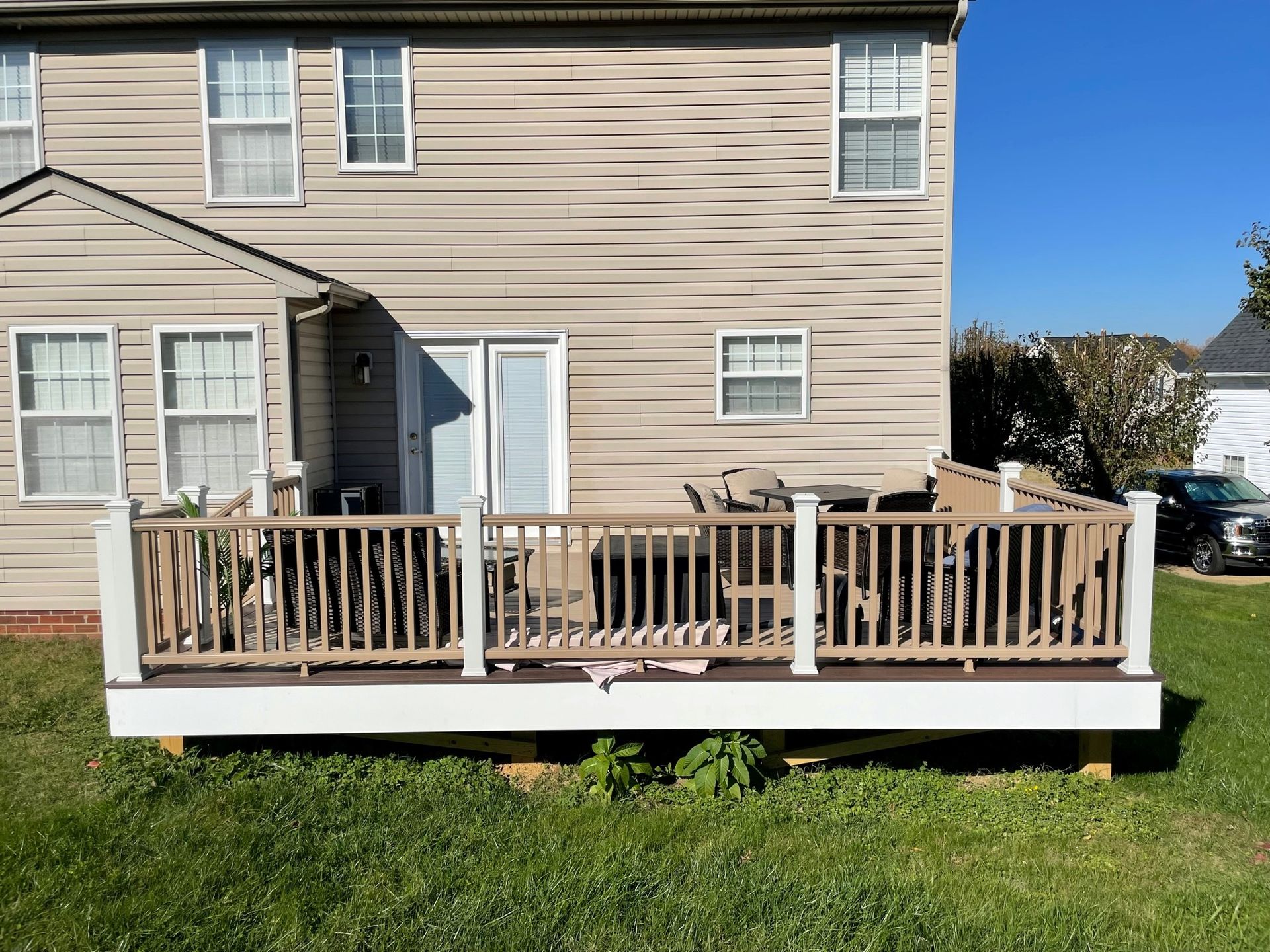 Backyard wooden deck attached to a beige house, with patio furniture and green lawn.