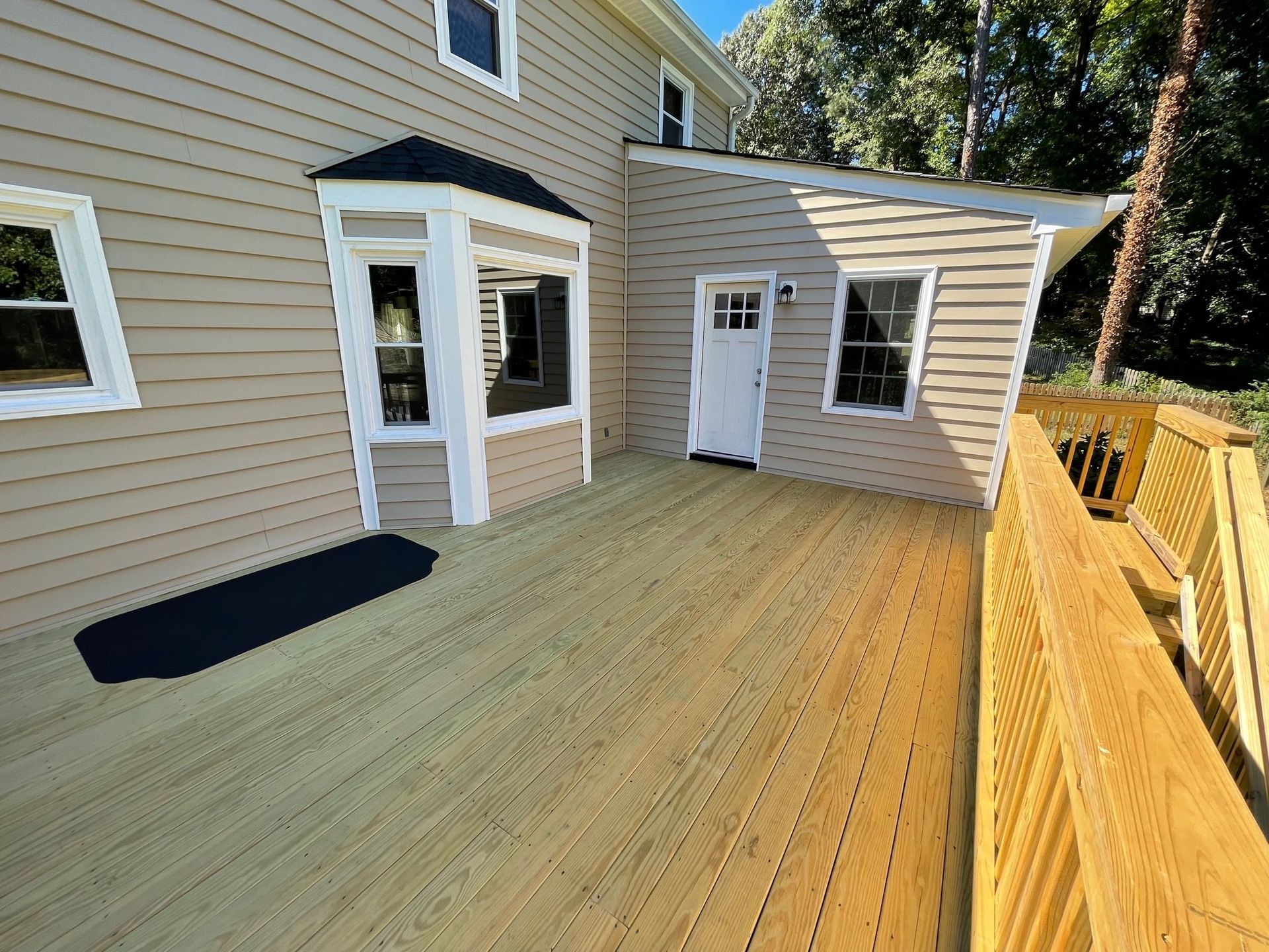 Back deck with beige siding, white doors, and wooden railing in a sunny backyard