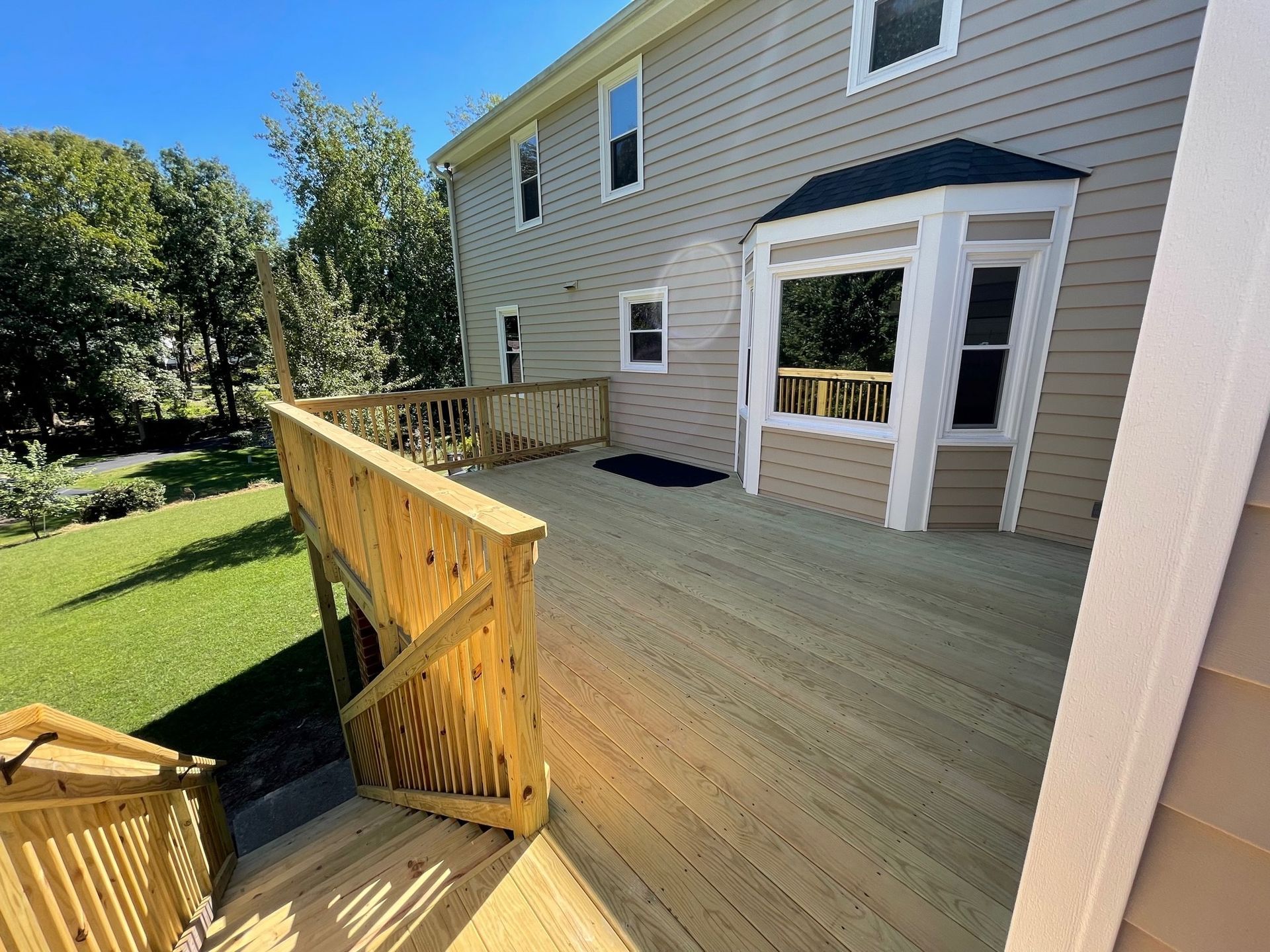 Back deck with wooden railing, beige house siding, and a screened porch door opening to a grassy yard