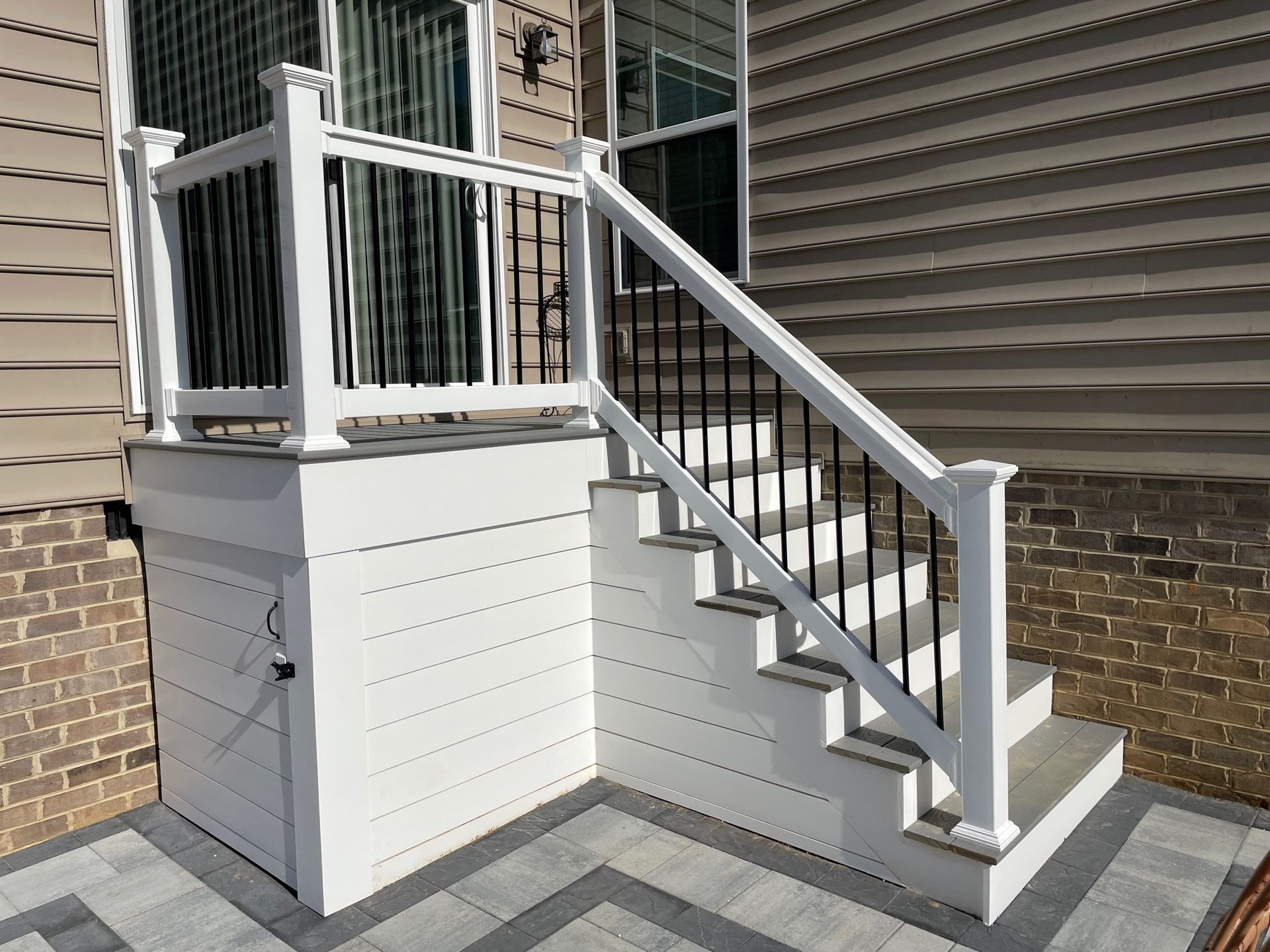 White accessible staircase and porch with railing beside a brick house.
