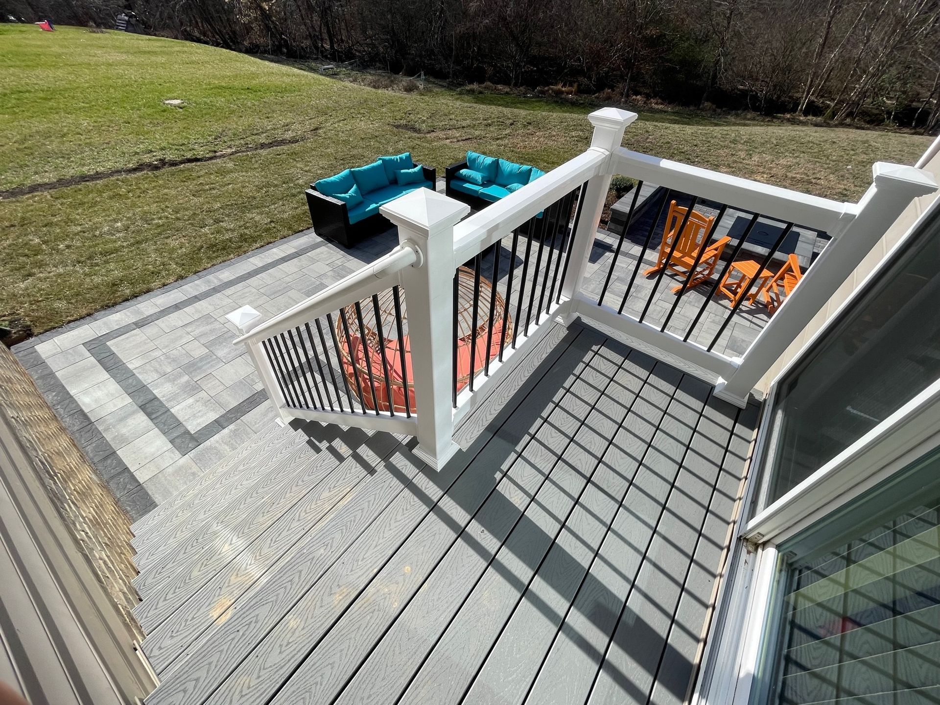 Wooden deck with white railings, gray flooring, and teal chairs overlooking a grassy yard.