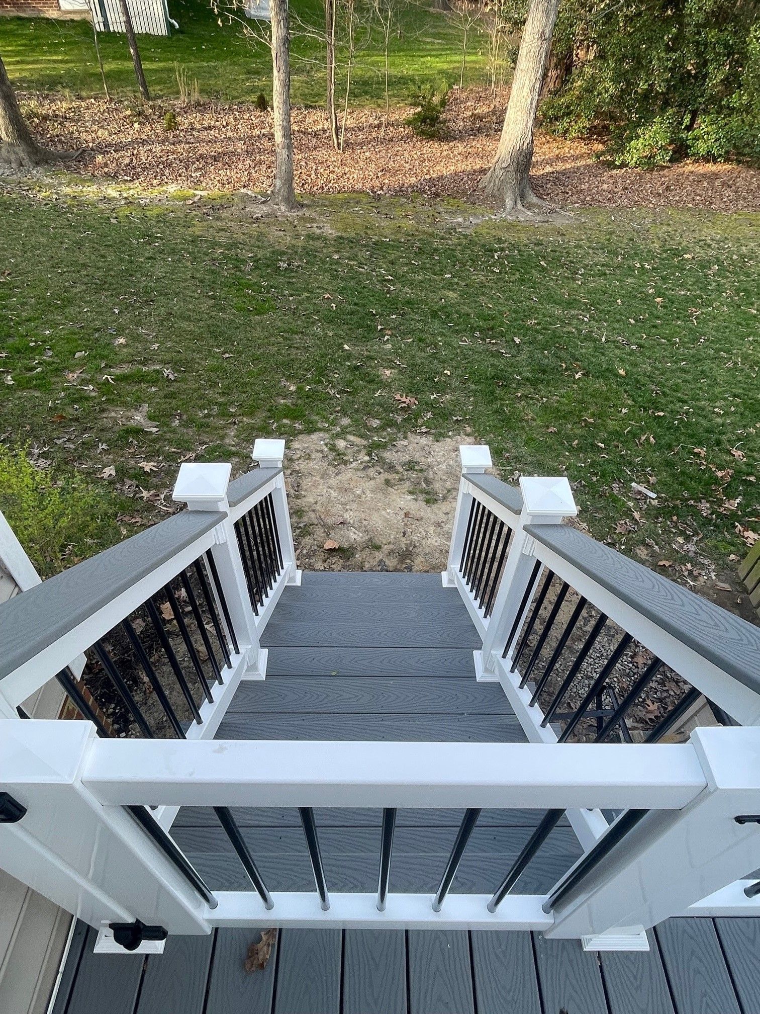 View from a porch down gray steps to a grassy yard with trees and fallen leaves.