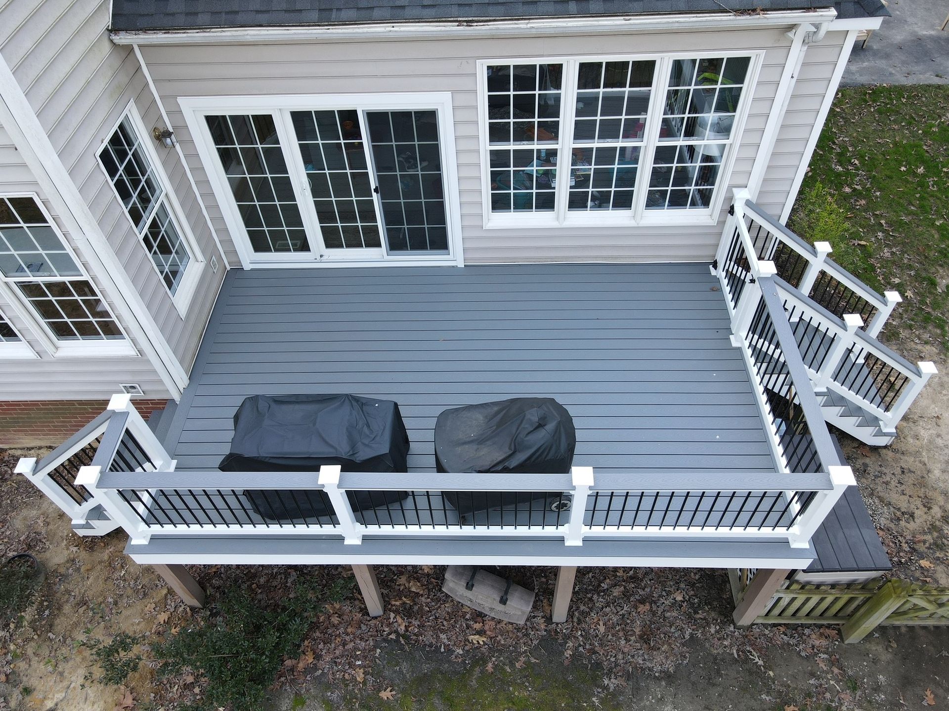 Wooden backyard deck with two covered grills, white railing, and sliding glass doors to the house