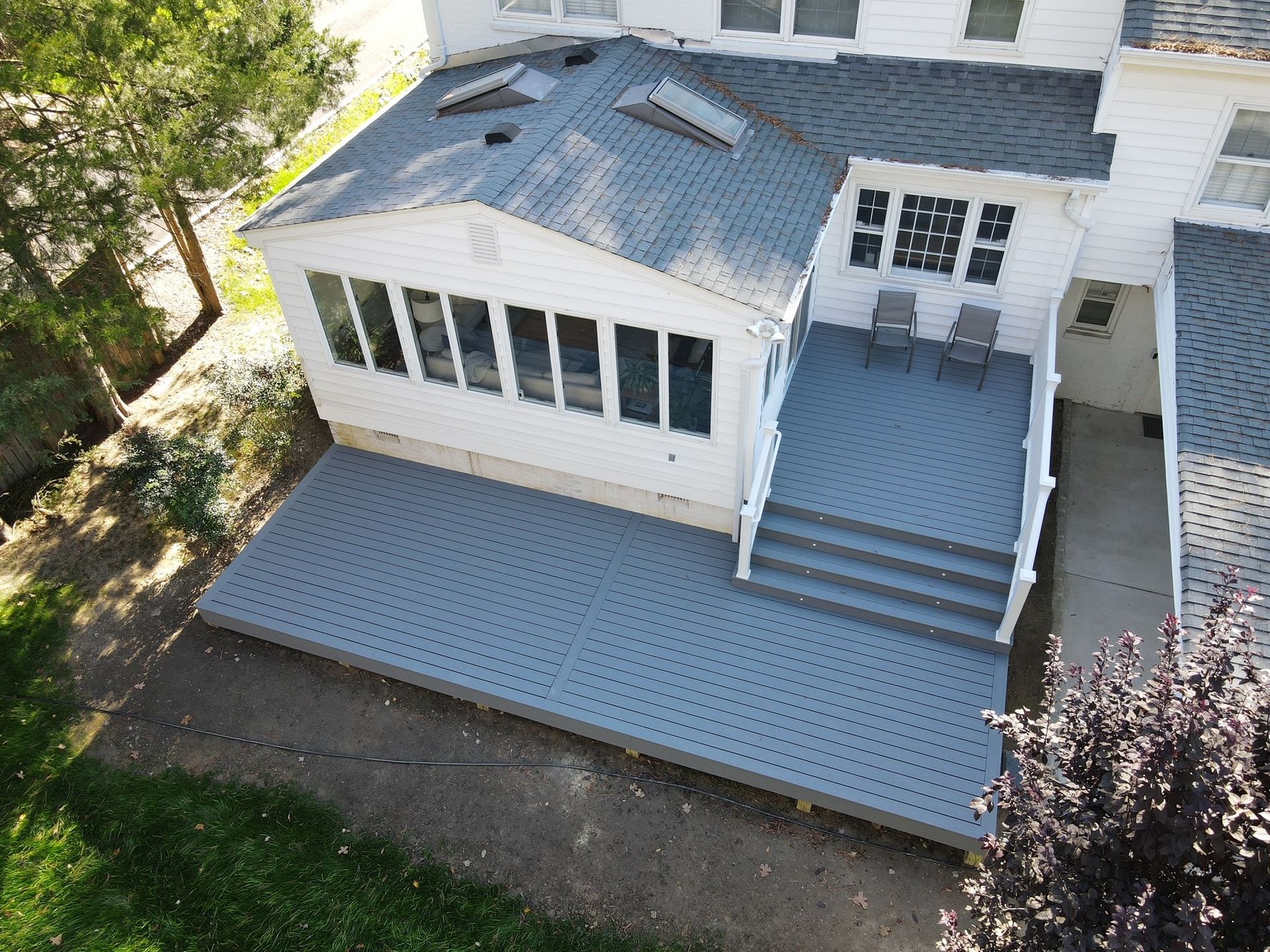 White house rear deck with blue steps, railing, and a screened porch overlooking a grassy yard.