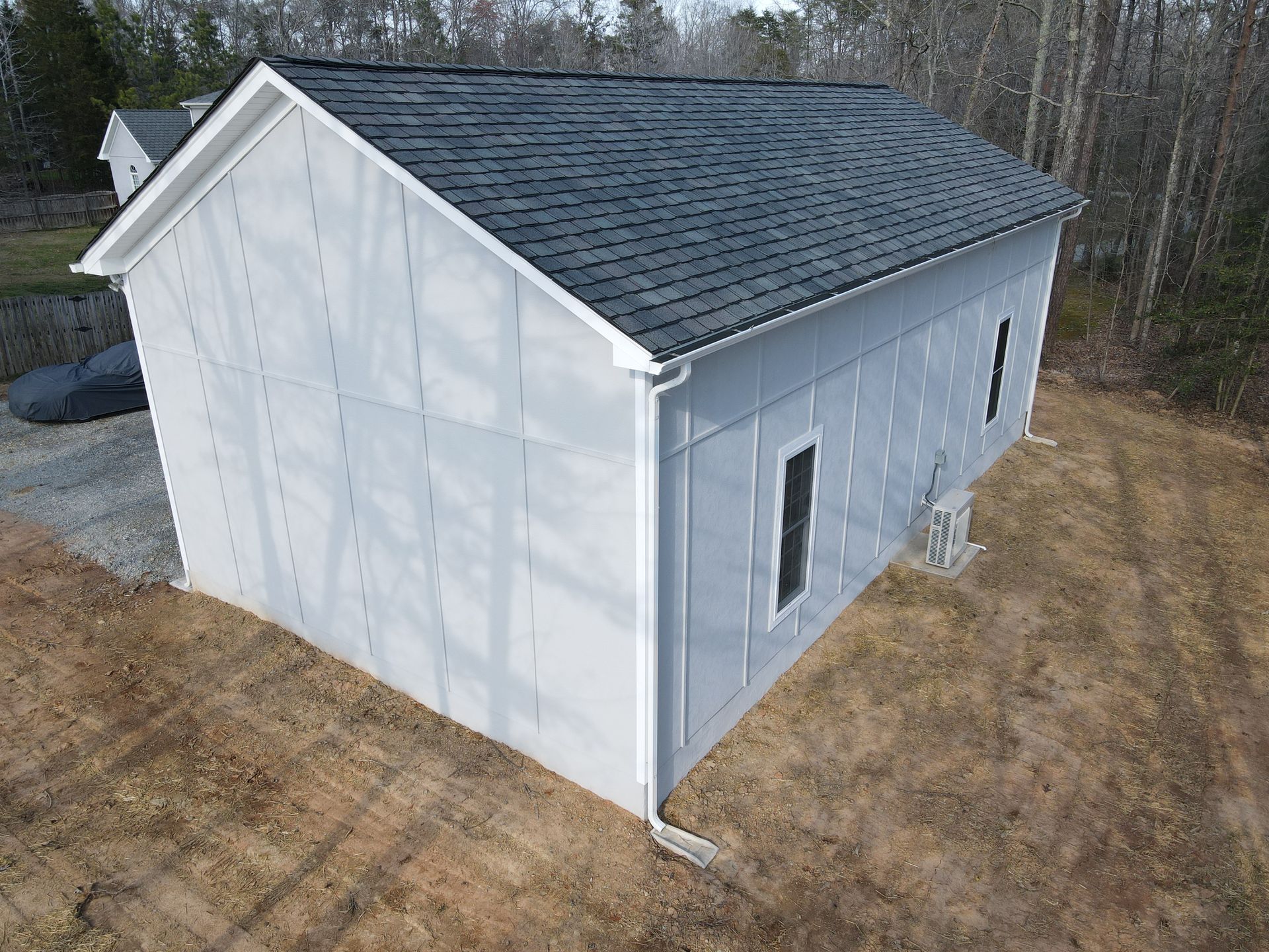 White unfinished house exterior with gray roof, viewed from the side on a grassy lot.