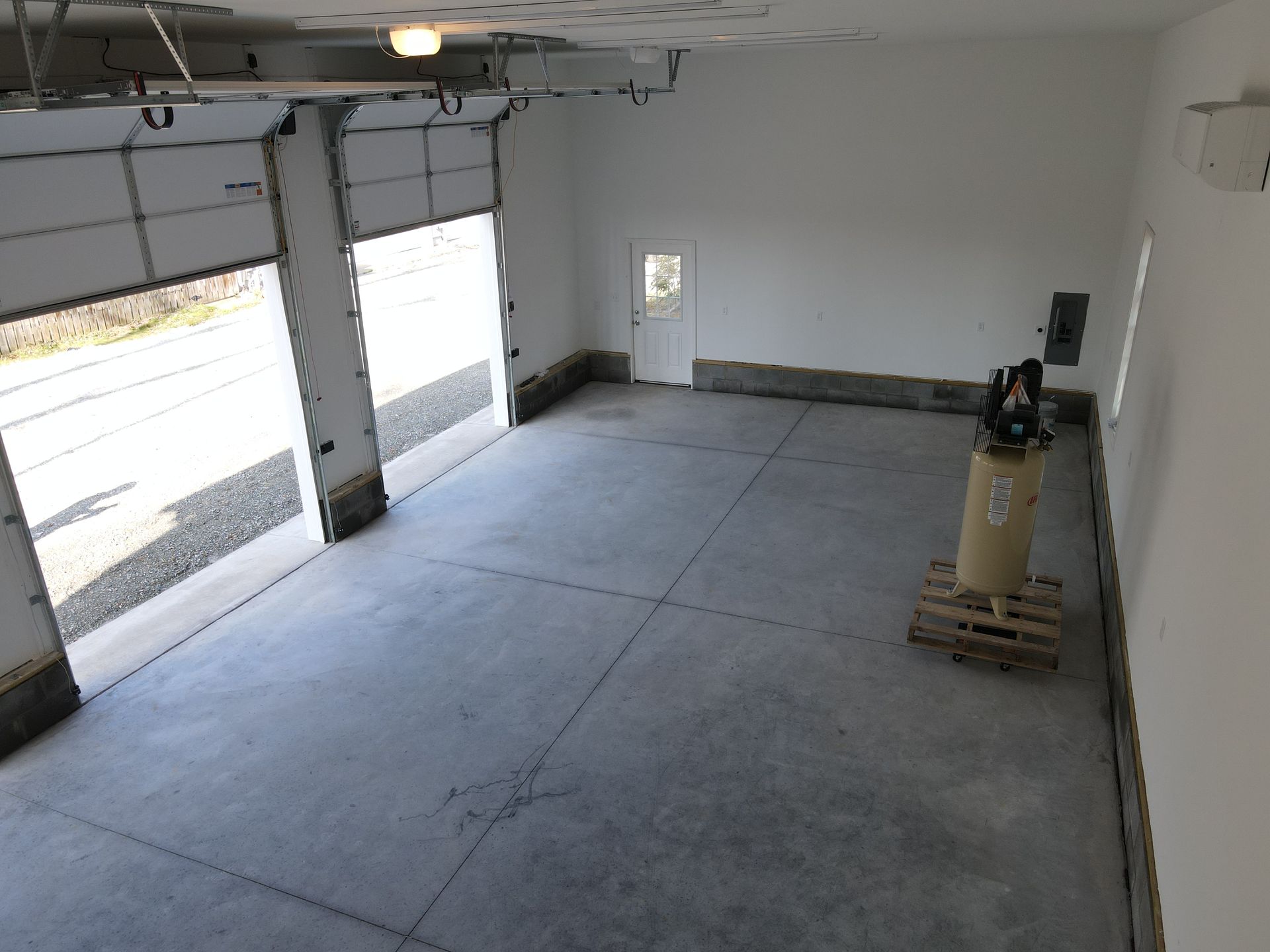 Empty garage with concrete floor, open doors, and a ladder standing near the right wall