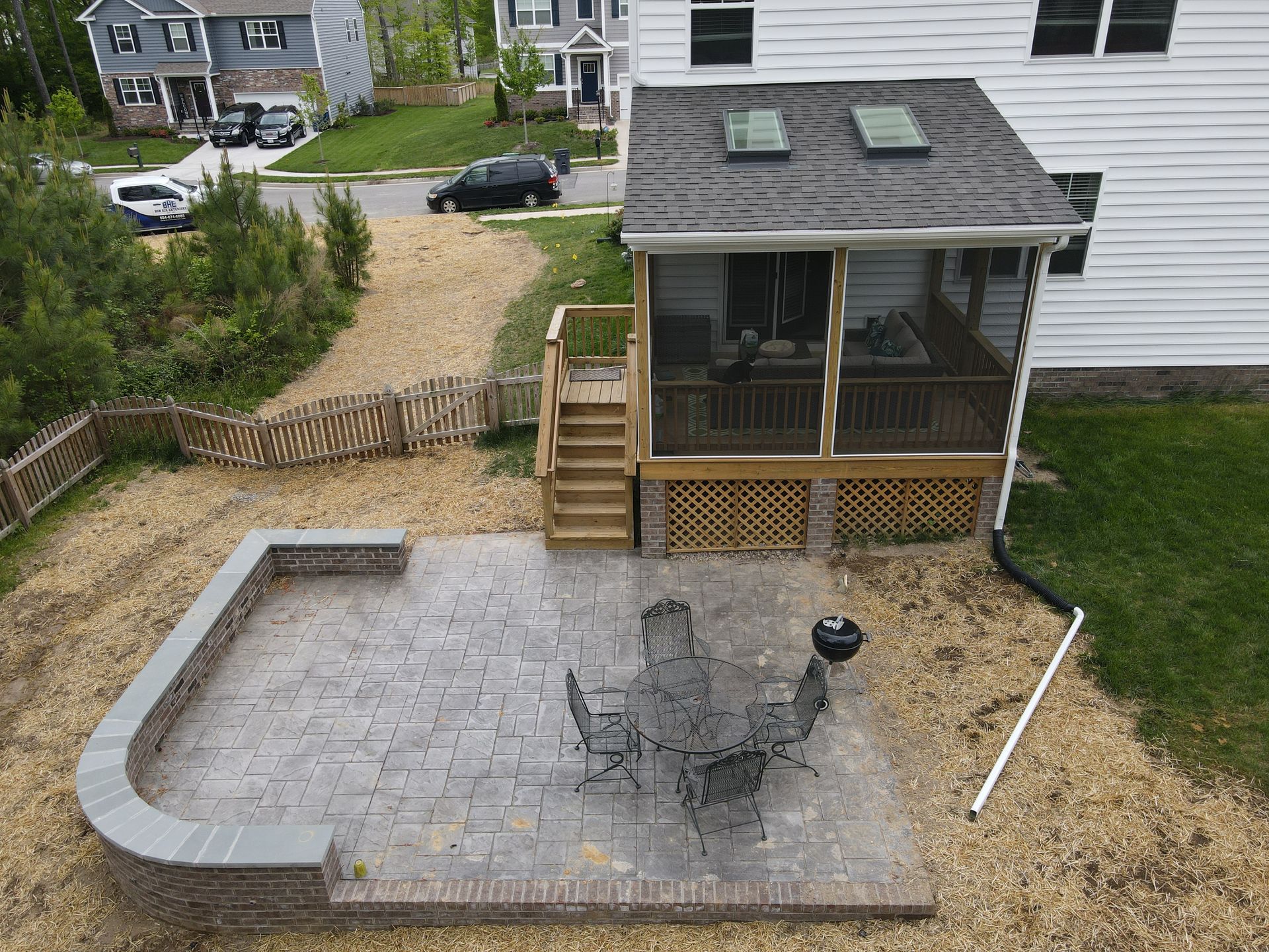 Backyard patio with stone pavers, outdoor table and chairs, wooden deck steps, and a fenced yard.