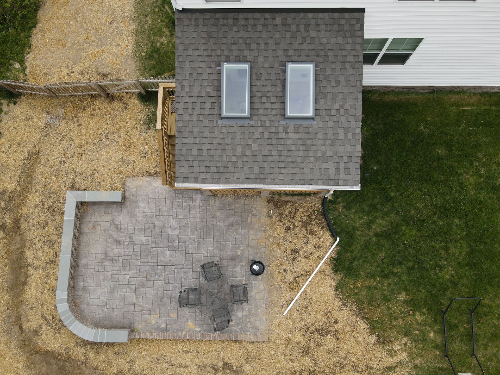 Overhead view of a backyard patio beside a house, with a small table and surrounding lawn.