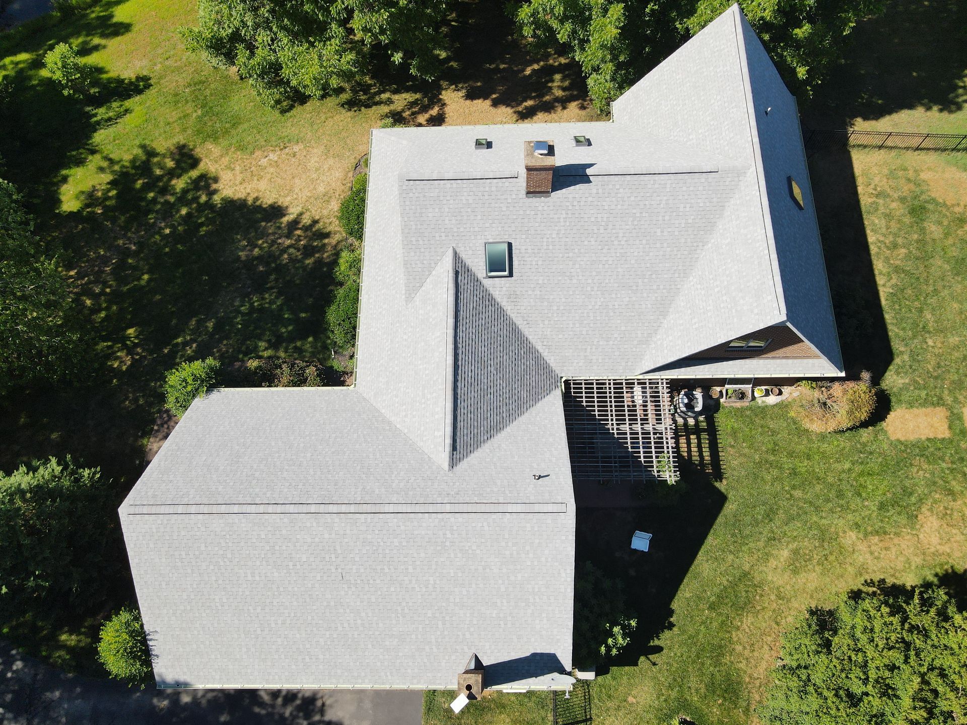 Aerial view of a gray-roofed house surrounded by green trees and lawn.