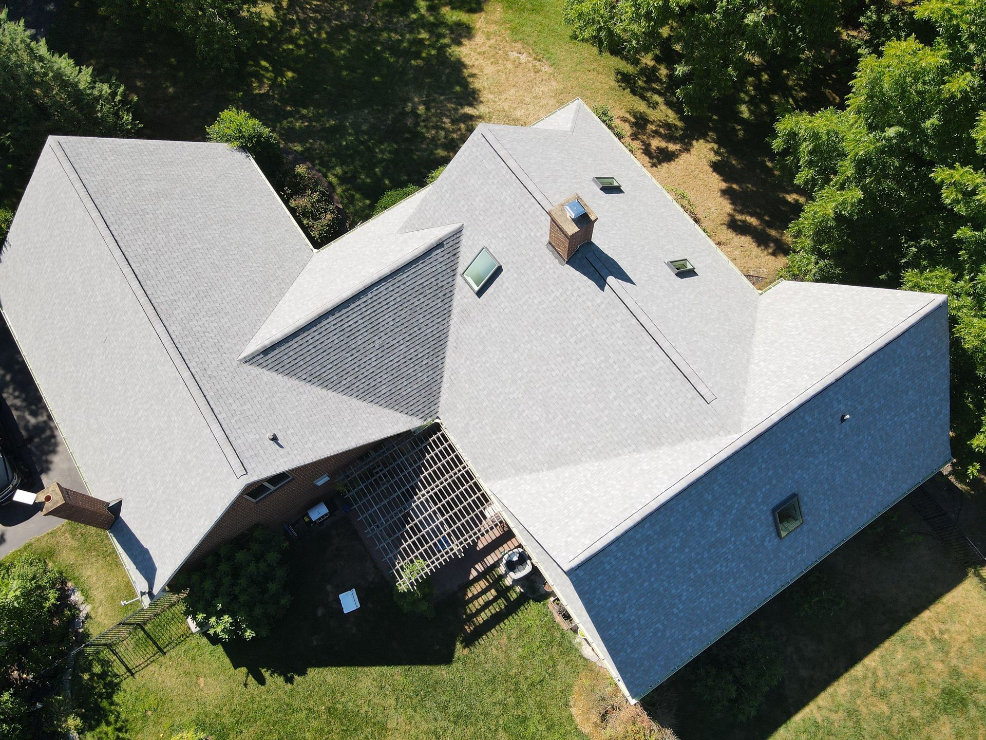 Aerial view of a gray-roofed house surrounded by green trees and lawn