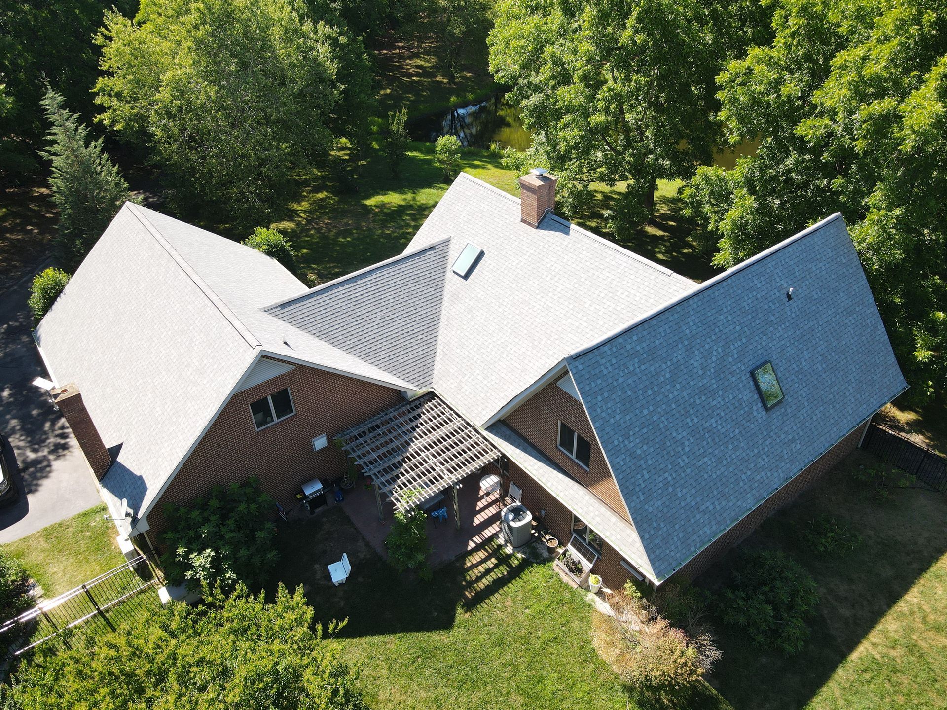 Aerial view of a gray-roofed house with wooden siding surrounded by green trees.