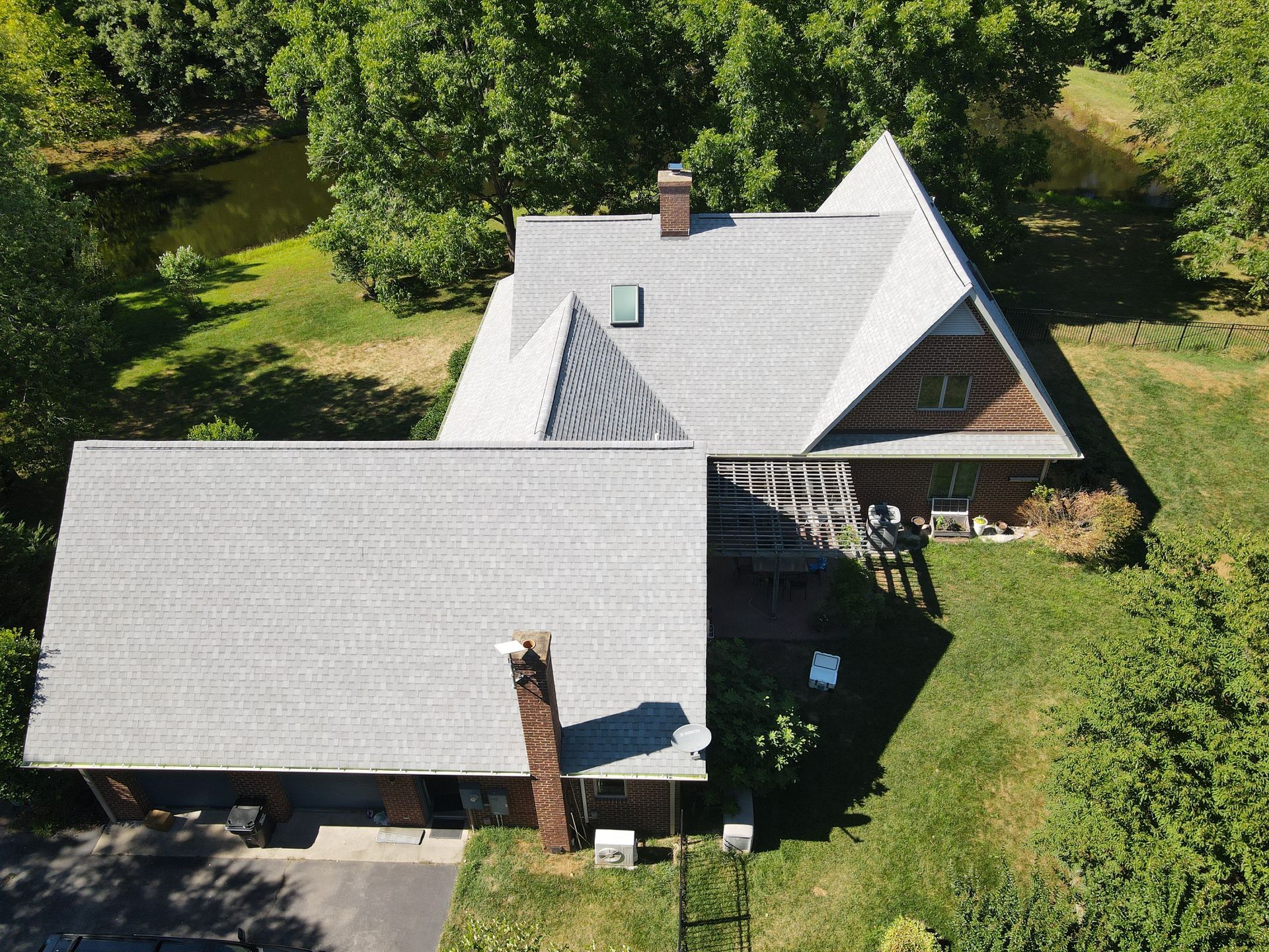 Aerial view of a house with gray roofs, a chimney, and a large grassy yard surrounded by trees.