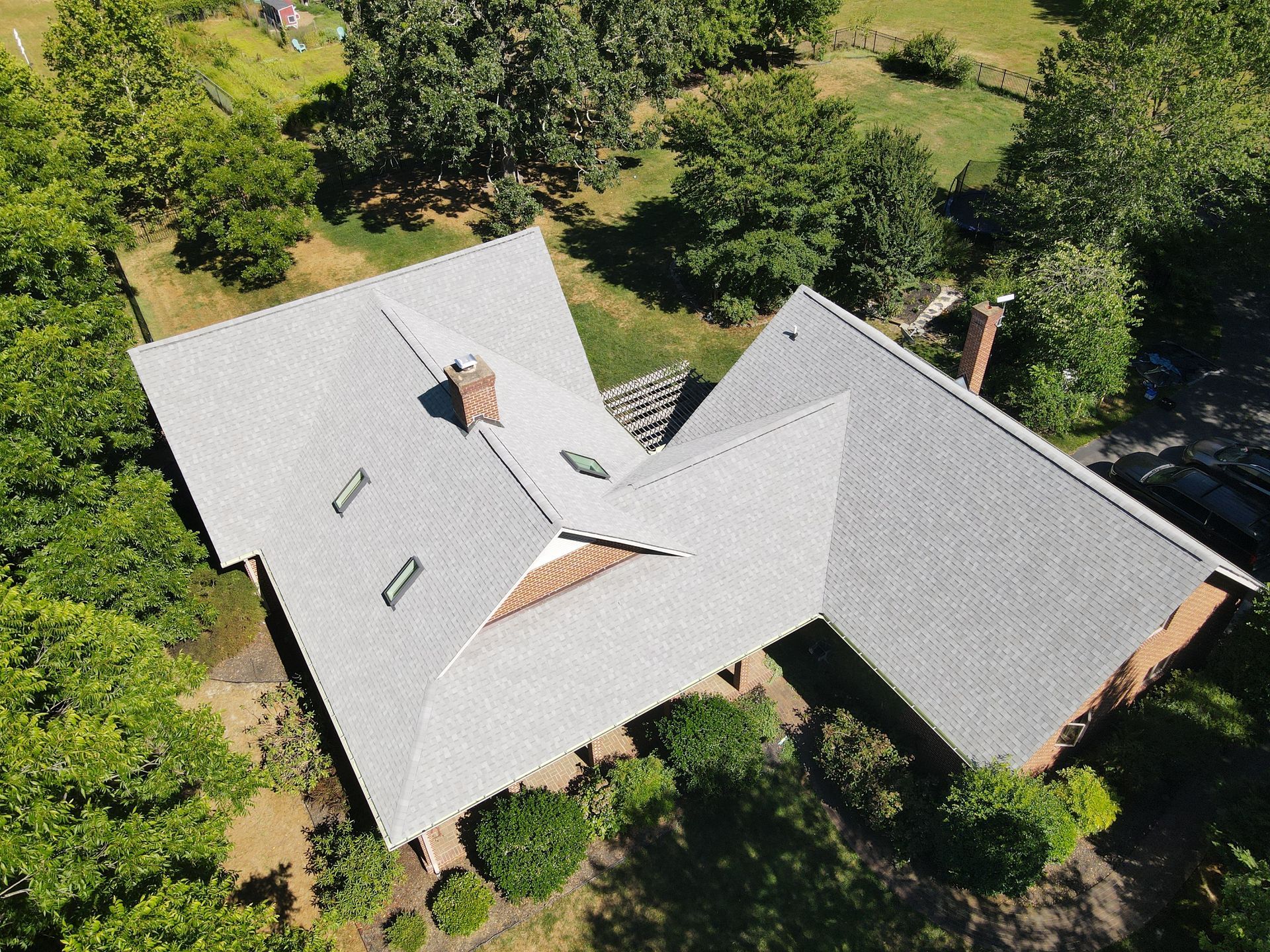 Aerial view of a house with a gray roof surrounded by green trees and lawn.