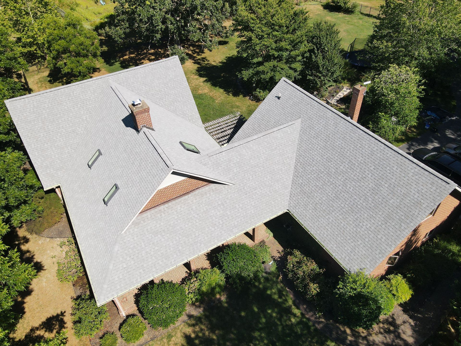 Aerial view of a gray-roofed house surrounded by green trees and lawn.
