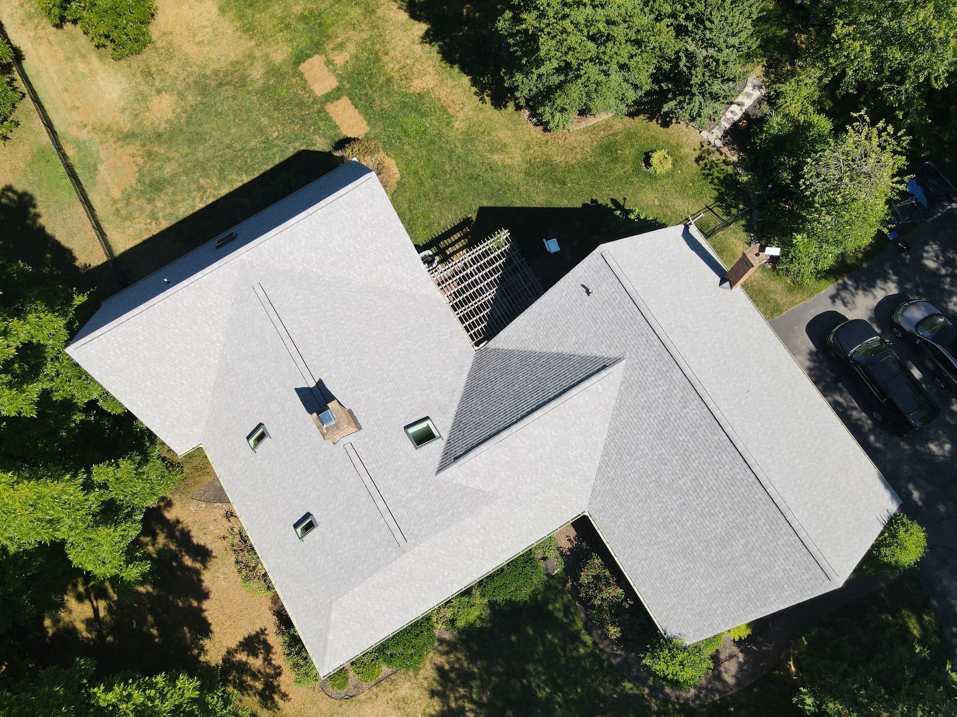 Aerial view of a house with a light gray roof surrounded by trees and grass