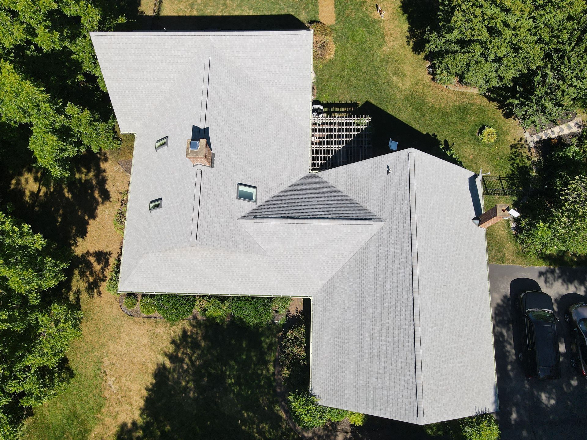 Aerial view of a gray-roofed house surrounded by green trees and grass