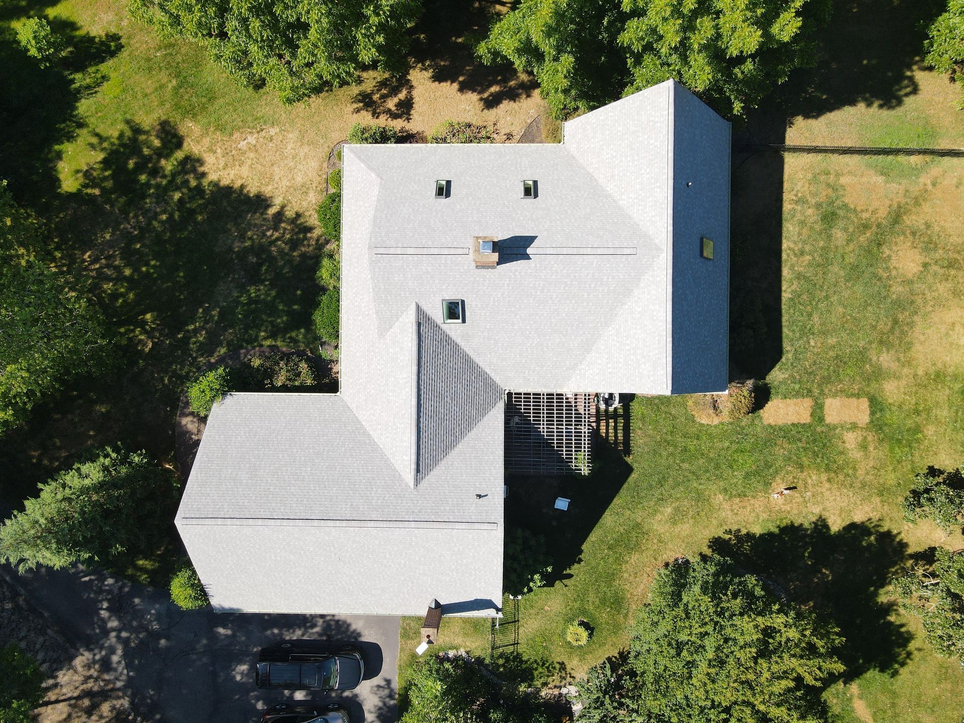 Aerial view of a house with a gray roof surrounded by green trees and lawn.