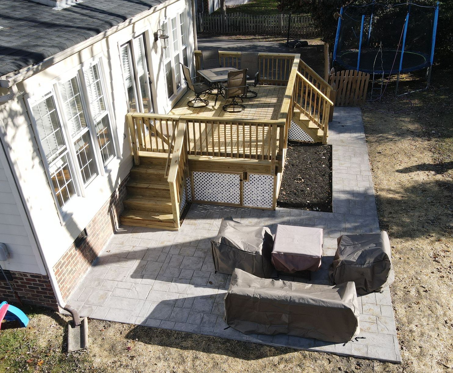 Backyard deck with wooden stairs, patio furniture, and a concrete patio beside a house