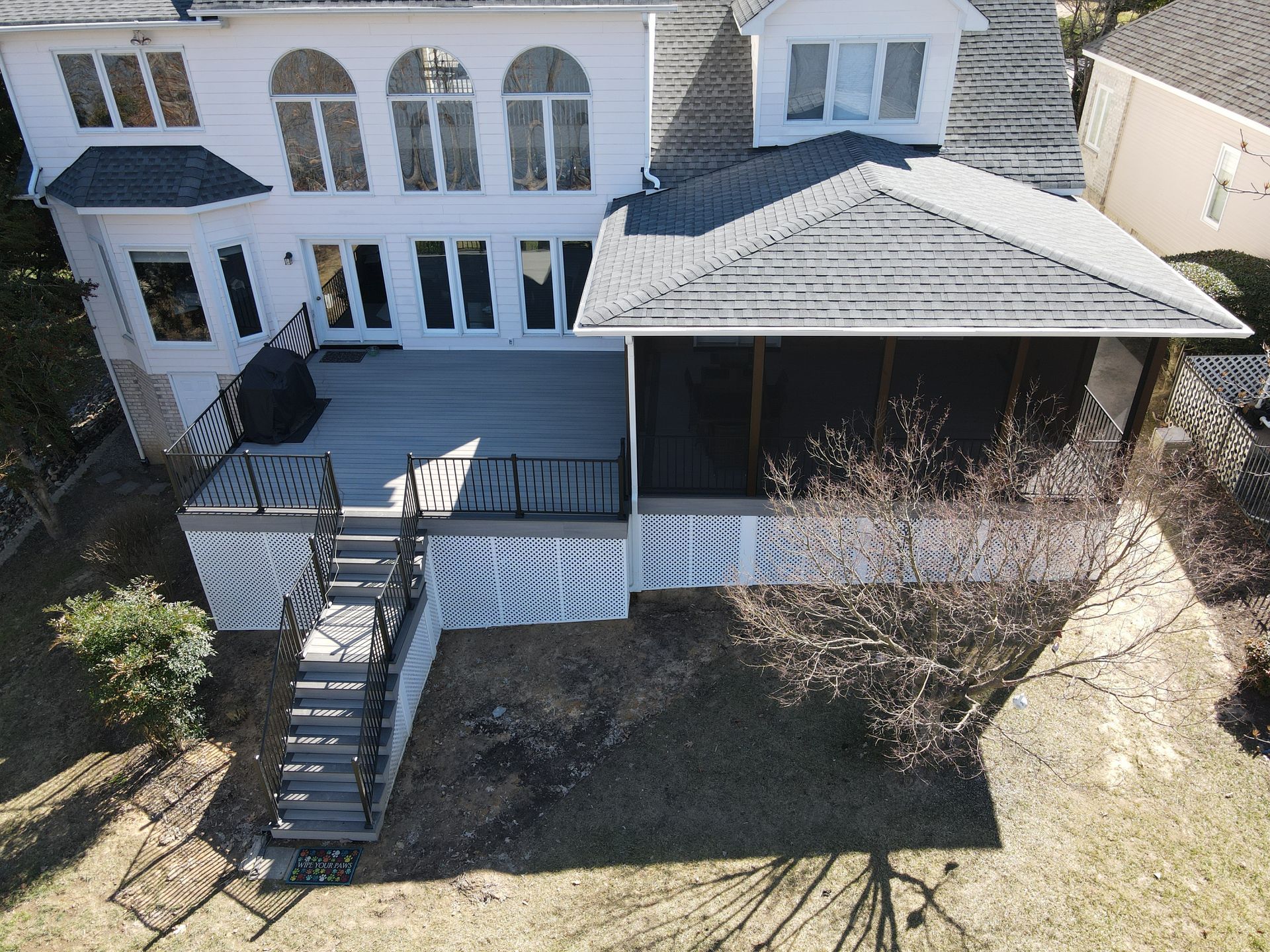 Rear view of a house with a raised deck, gray stairs, white railings, and a covered patio area