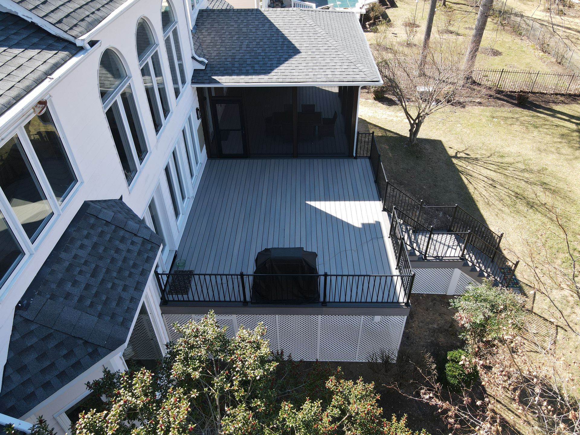 Back deck with white railing, gray flooring, and a covered porch beside a house and yard.