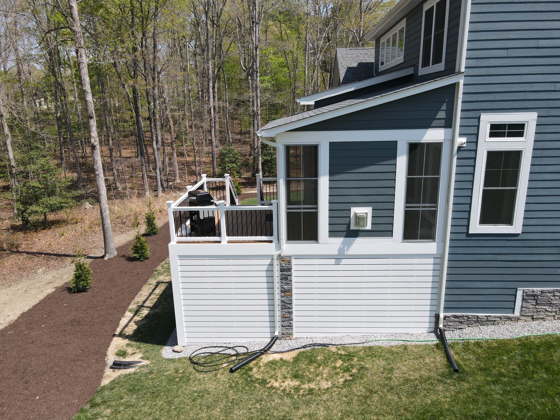 Blue house with a white screened porch and deck beside a wooded yard