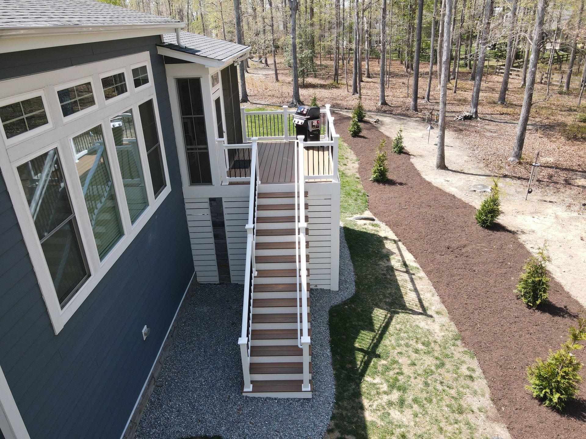 Exterior of a house with white stairs and railing, blue siding, gravel path, and landscaped yard