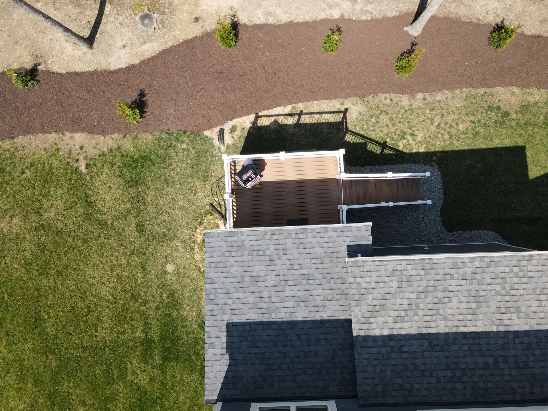 Aerial view of a house roof, small deck, lawn, and curved walkway with shrubs