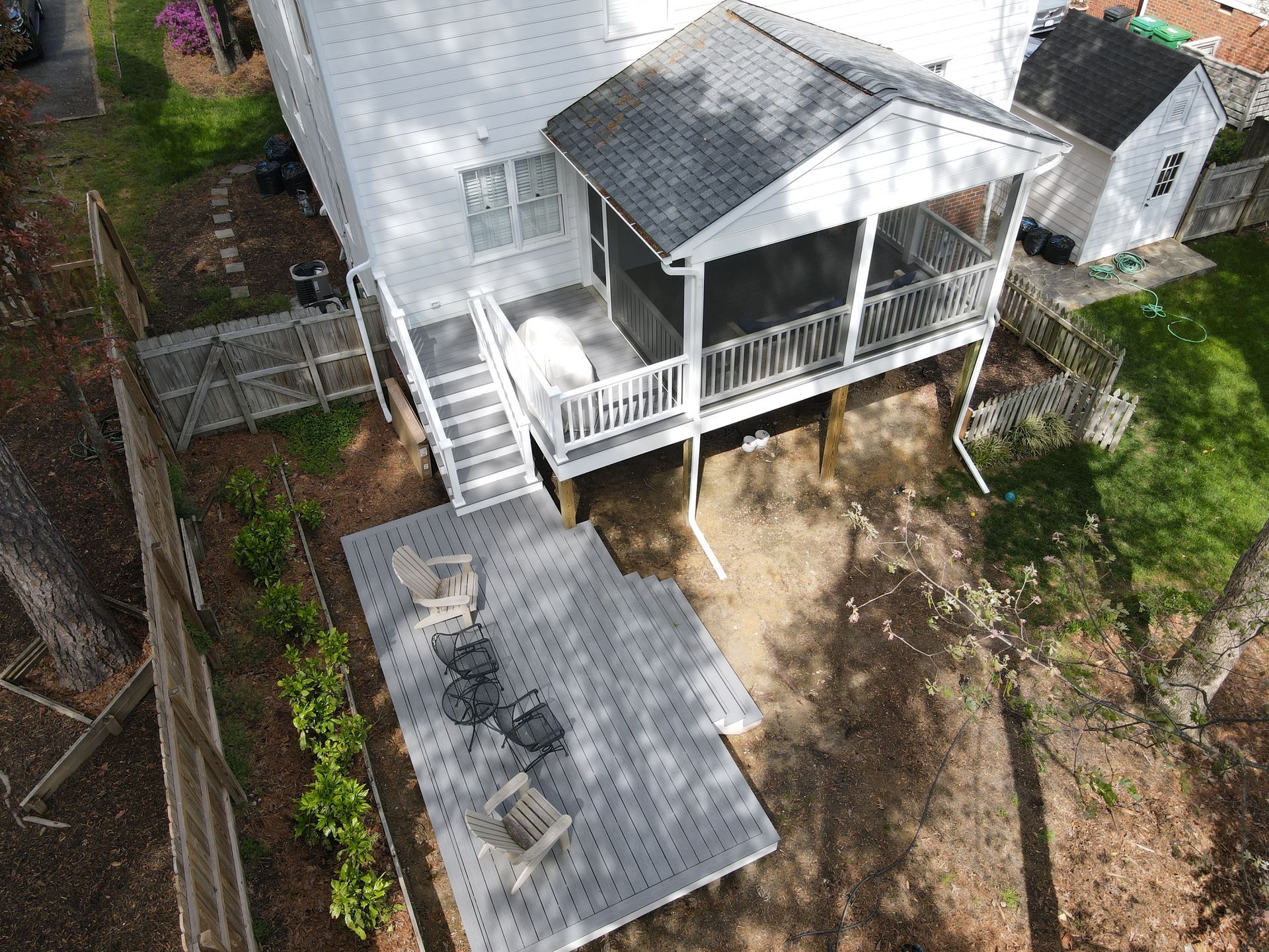 Aerial view of a white house with a wraparound porch and fenced yard, showing a gray roofed patio below.