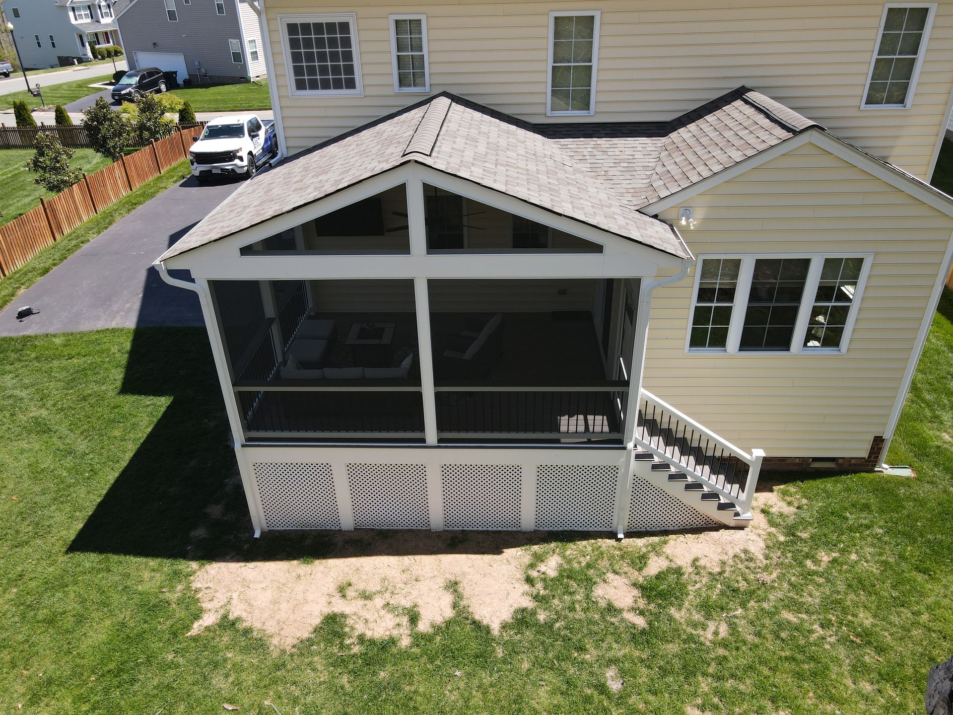 Backyard screened porch attached to a beige house, with white railings and steps leading down to the lawn.