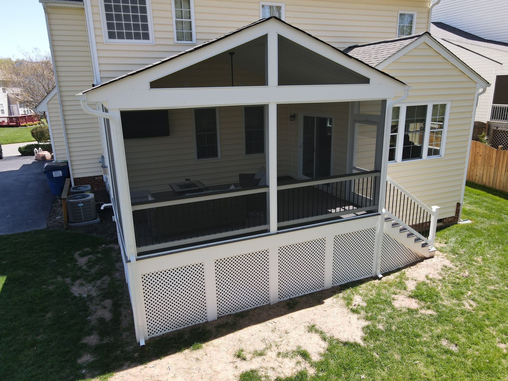 White screened porch with lattice skirting attached to a beige house, viewed from the yard.