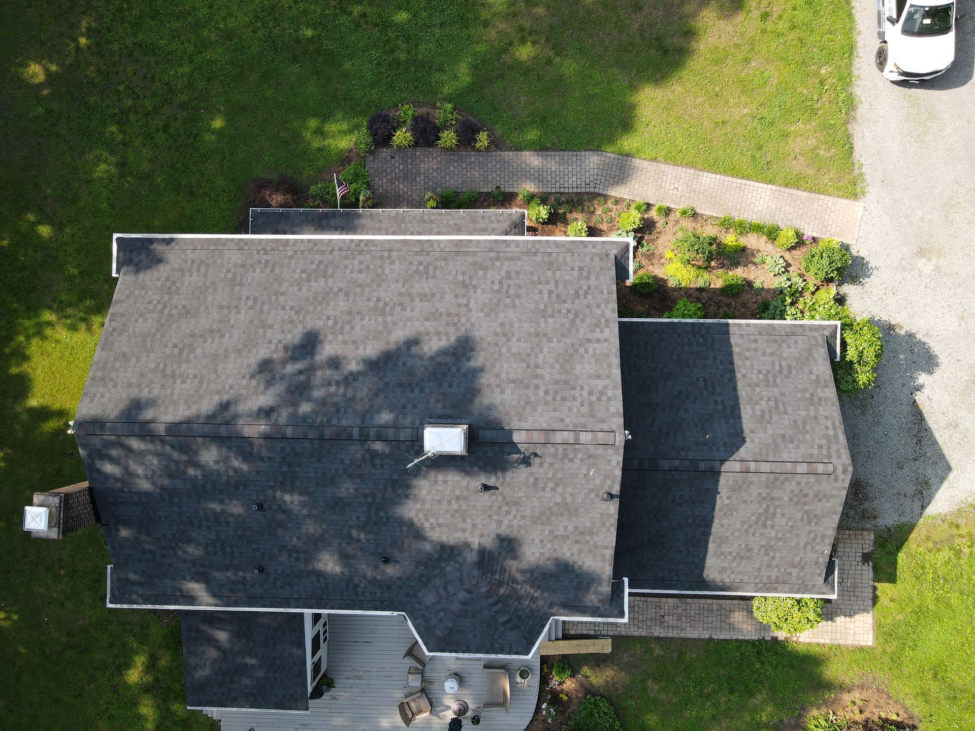 Aerial view of a gray-roofed house with surrounding lawn, driveway, and trees.