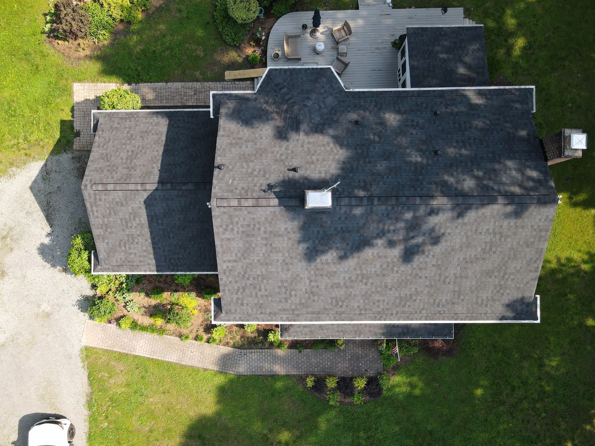 Aerial view of a gray-roofed house with a small yard and driveway surrounded by grass and trees