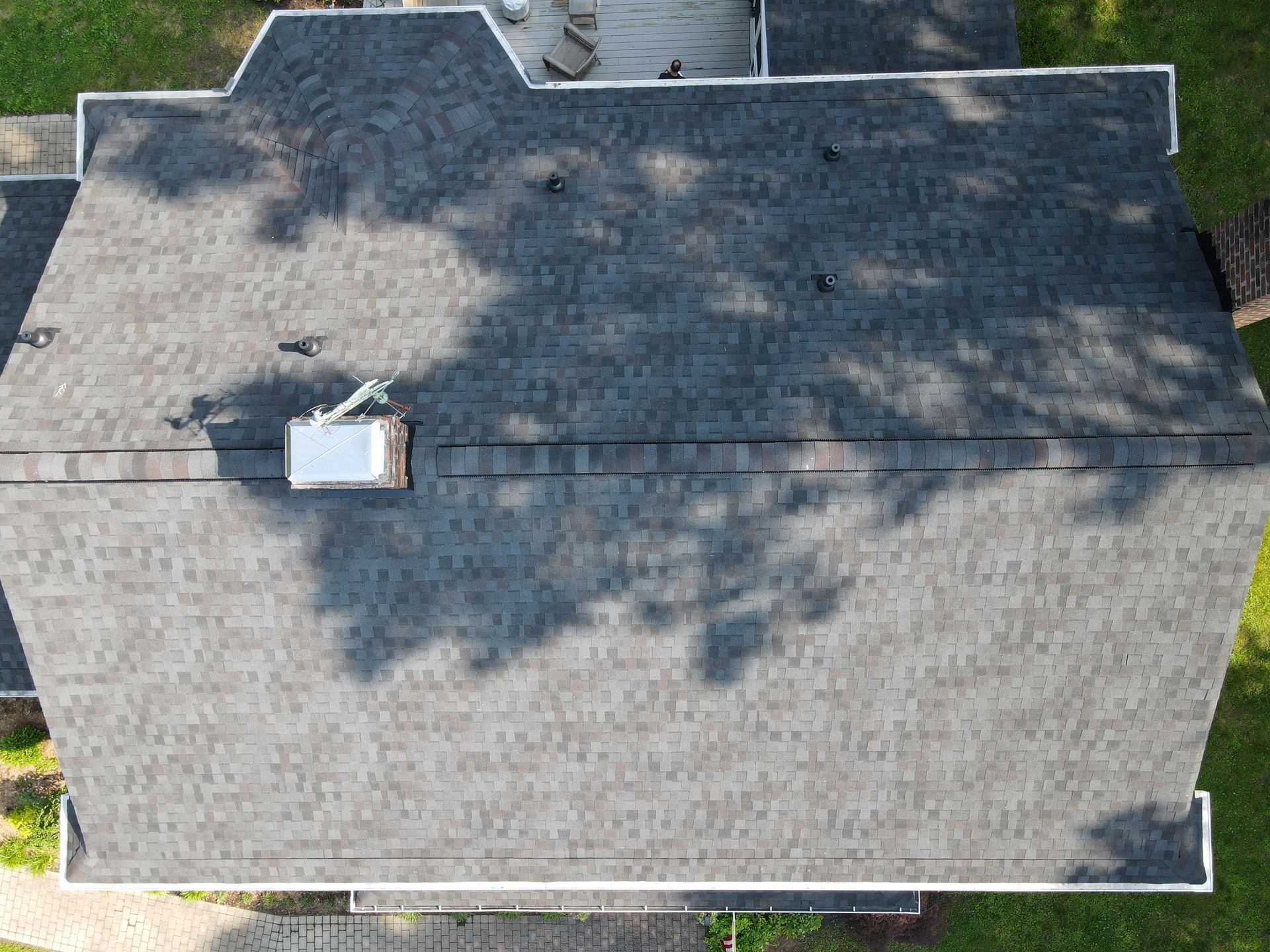 Aerial view of a gray shingled house roof with a skylight and tree shadows.