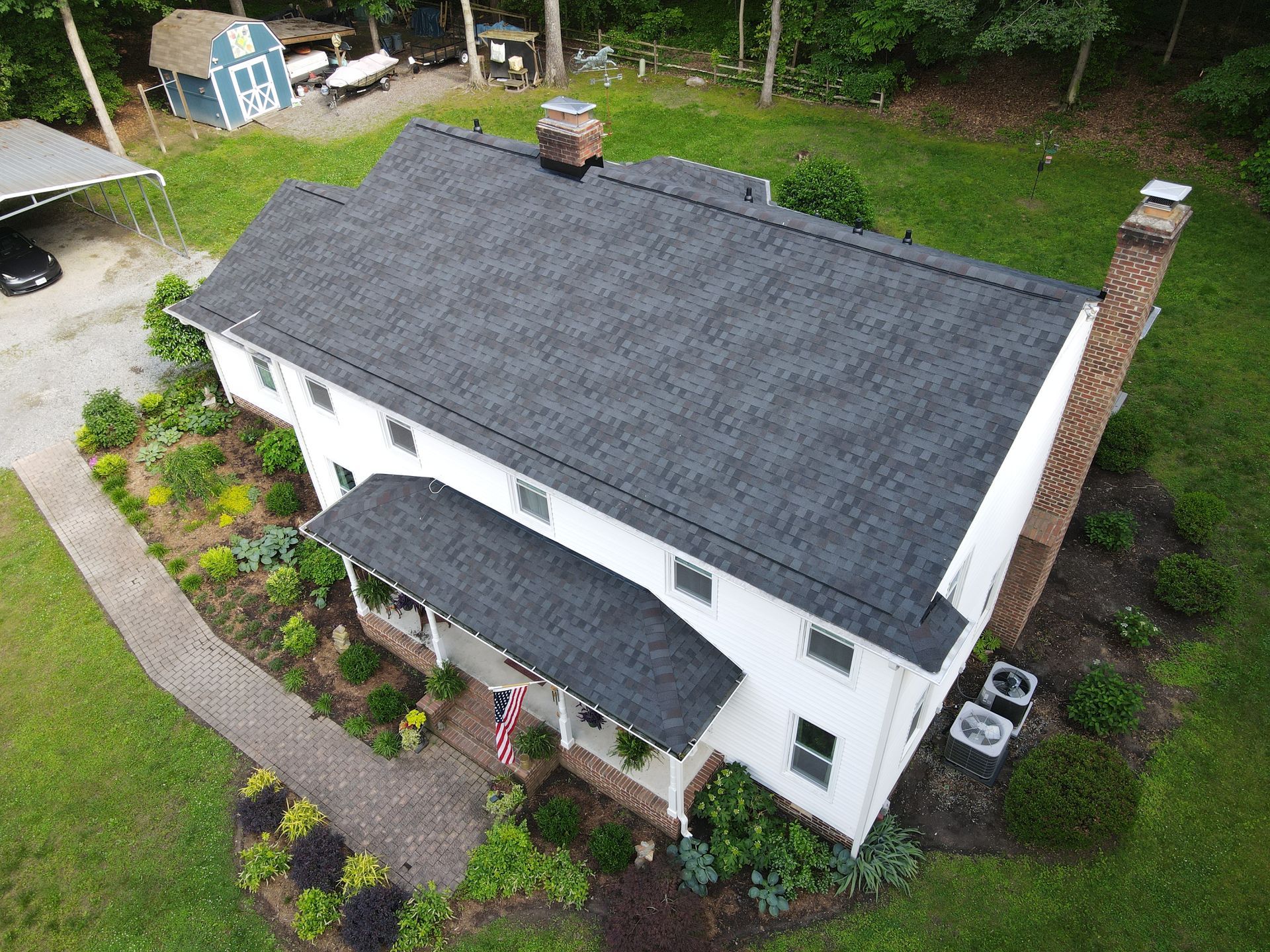 Aerial view of a white house with a dark roof, surrounded by green landscaping and a curved walkway