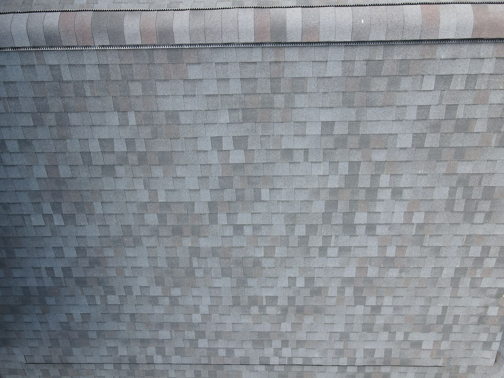 Close-up of a gray shingled roof with a small black cable hanging from the bottom edge.