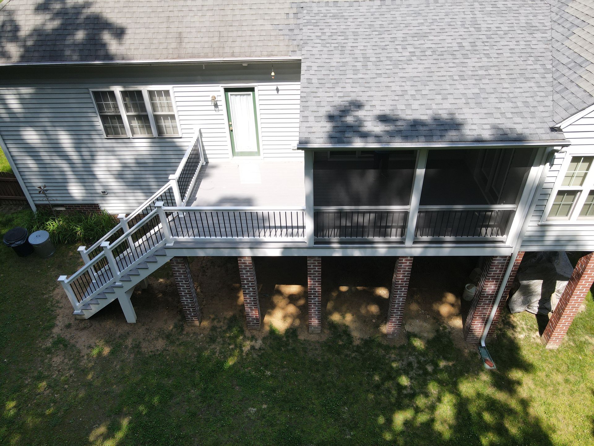 Raised white porch with stairs and railing on a house, viewed from above, with grass below