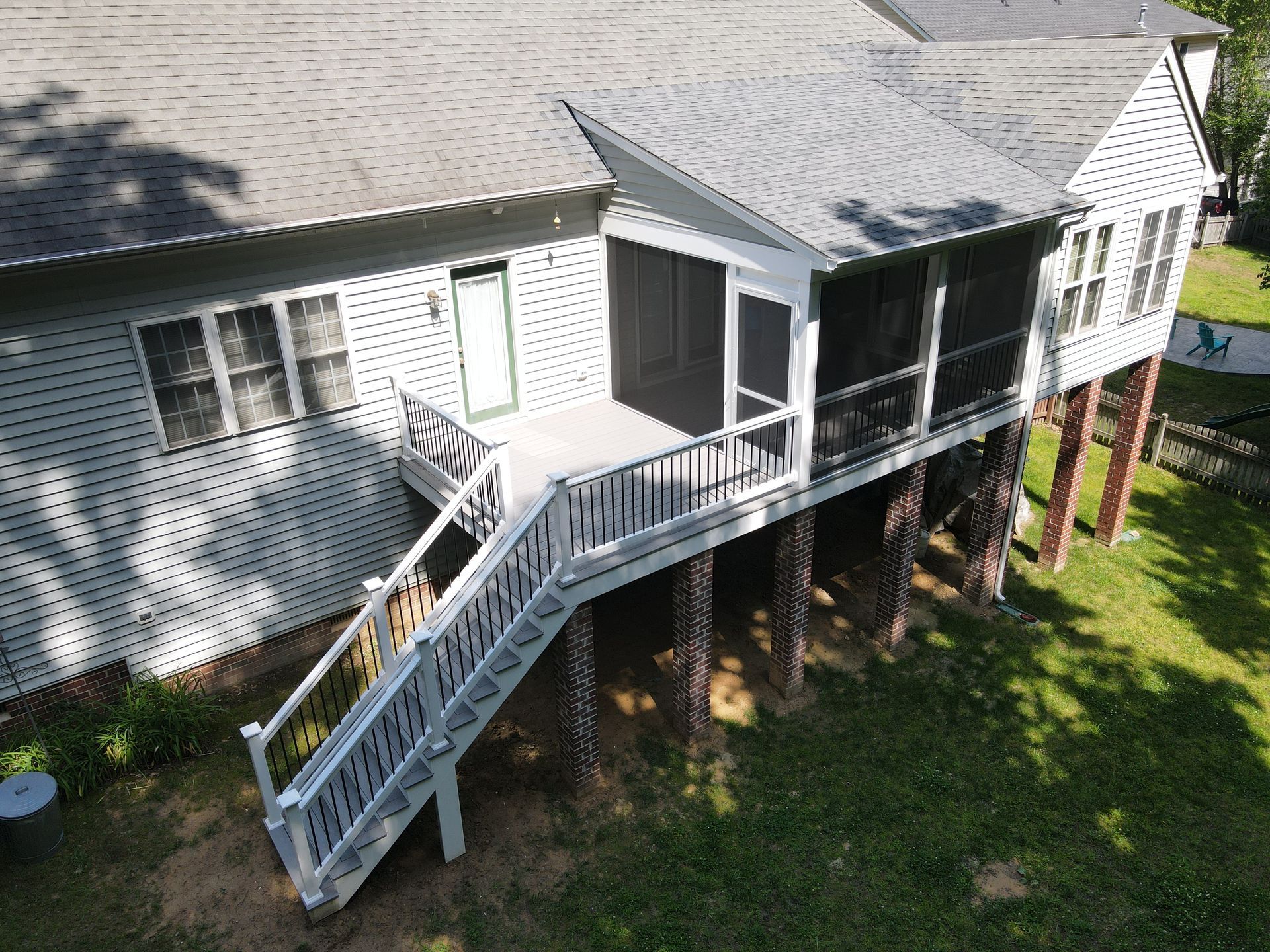 White house with a raised deck and exterior staircase in a grassy yard, viewed from above.