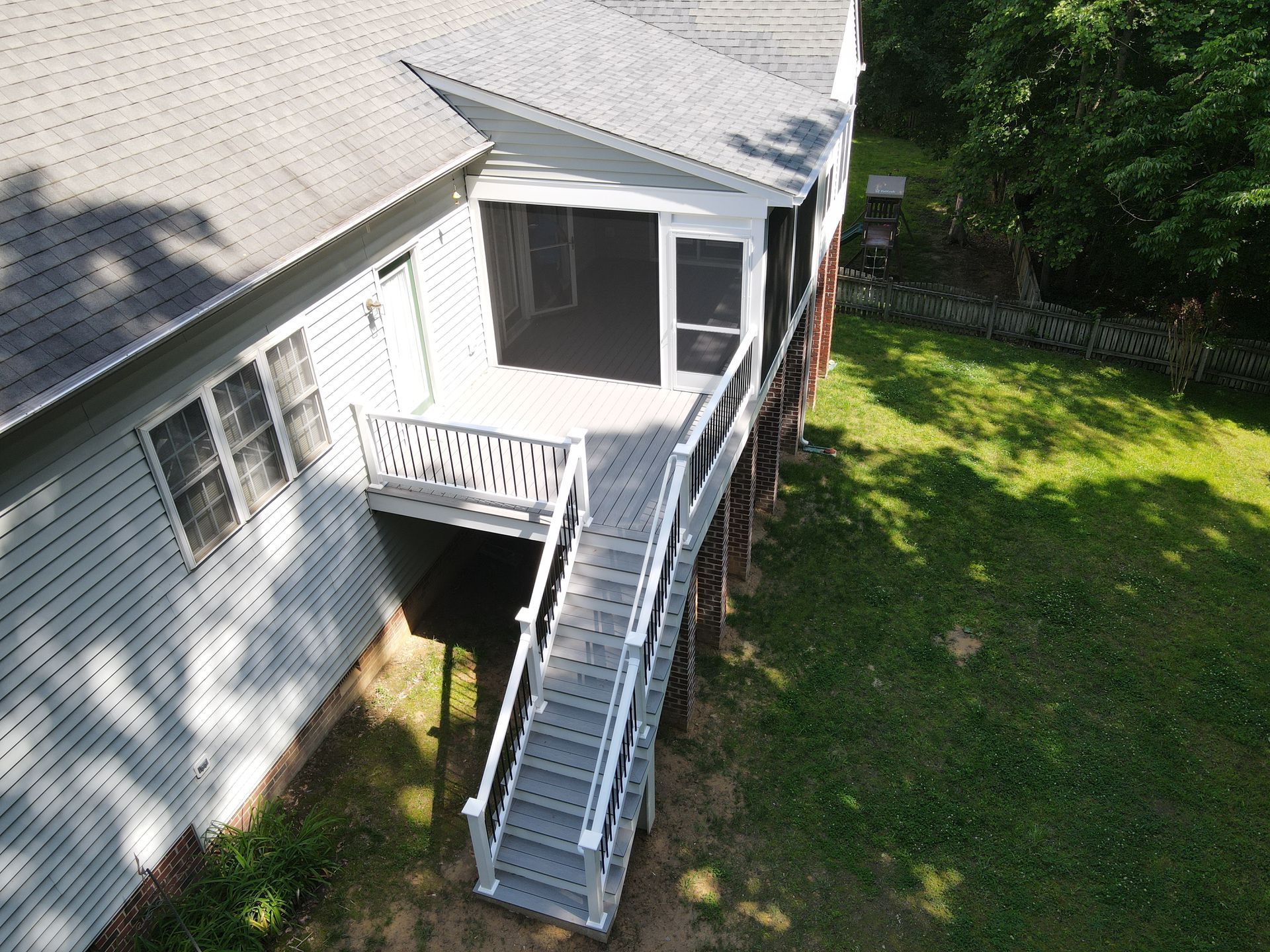 Aerial view of a house with a white staircase leading to an elevated back porch and green lawn below.