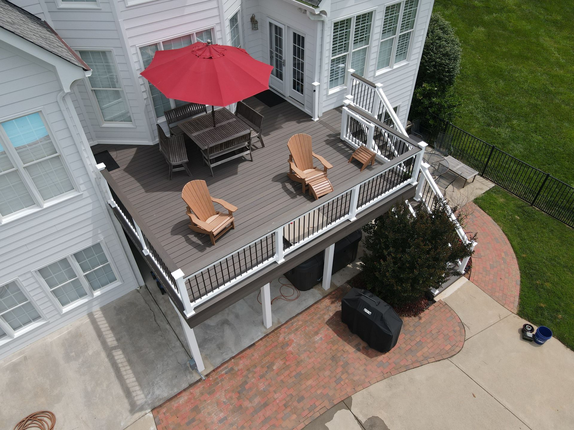 Elevated deck with red umbrella, lounge chairs, table, and grill beside a house and brick patio