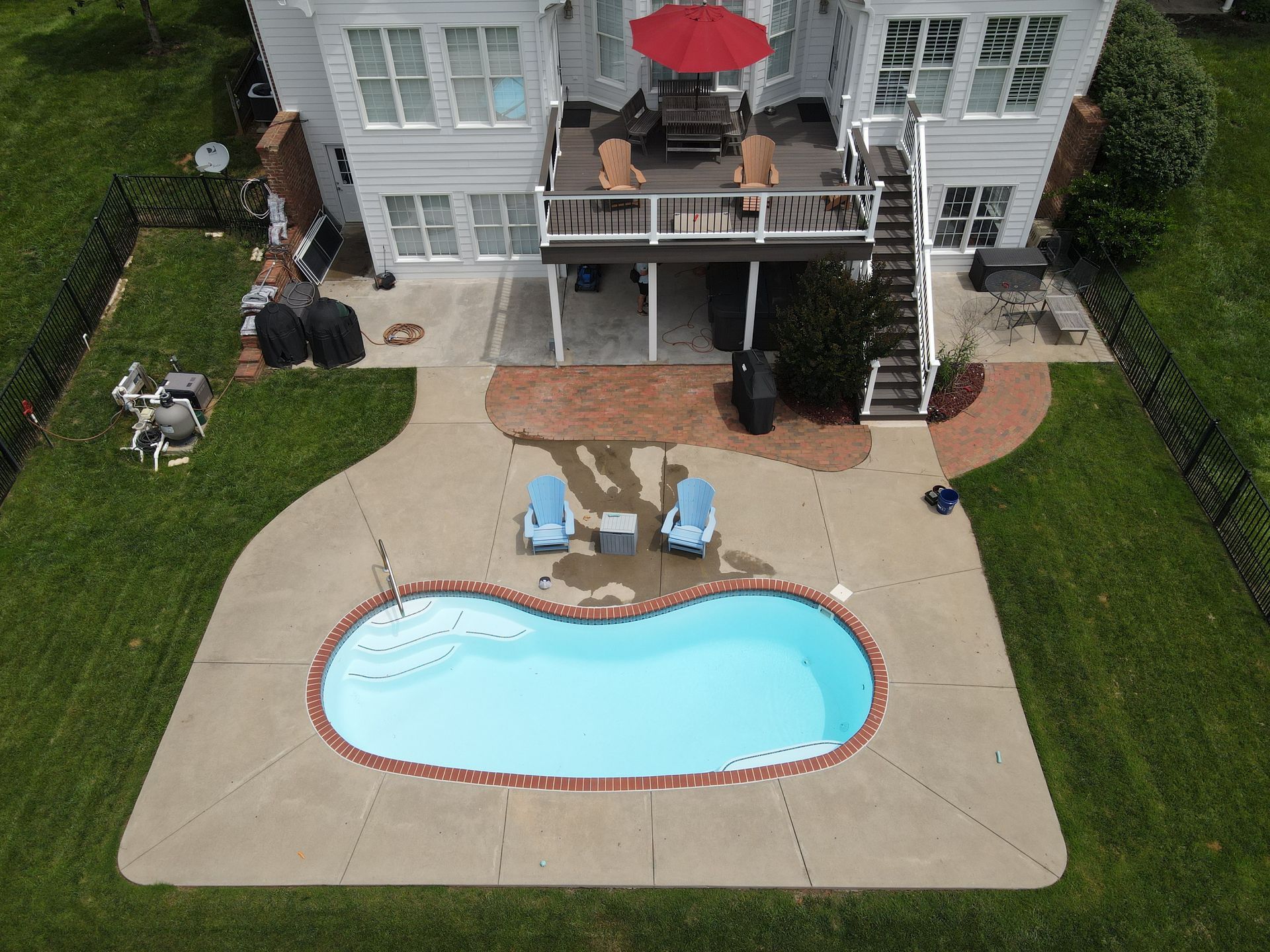 Backyard with kidney-shaped swimming pool, patio chairs, and a two-story house with a deck and red umbrella.