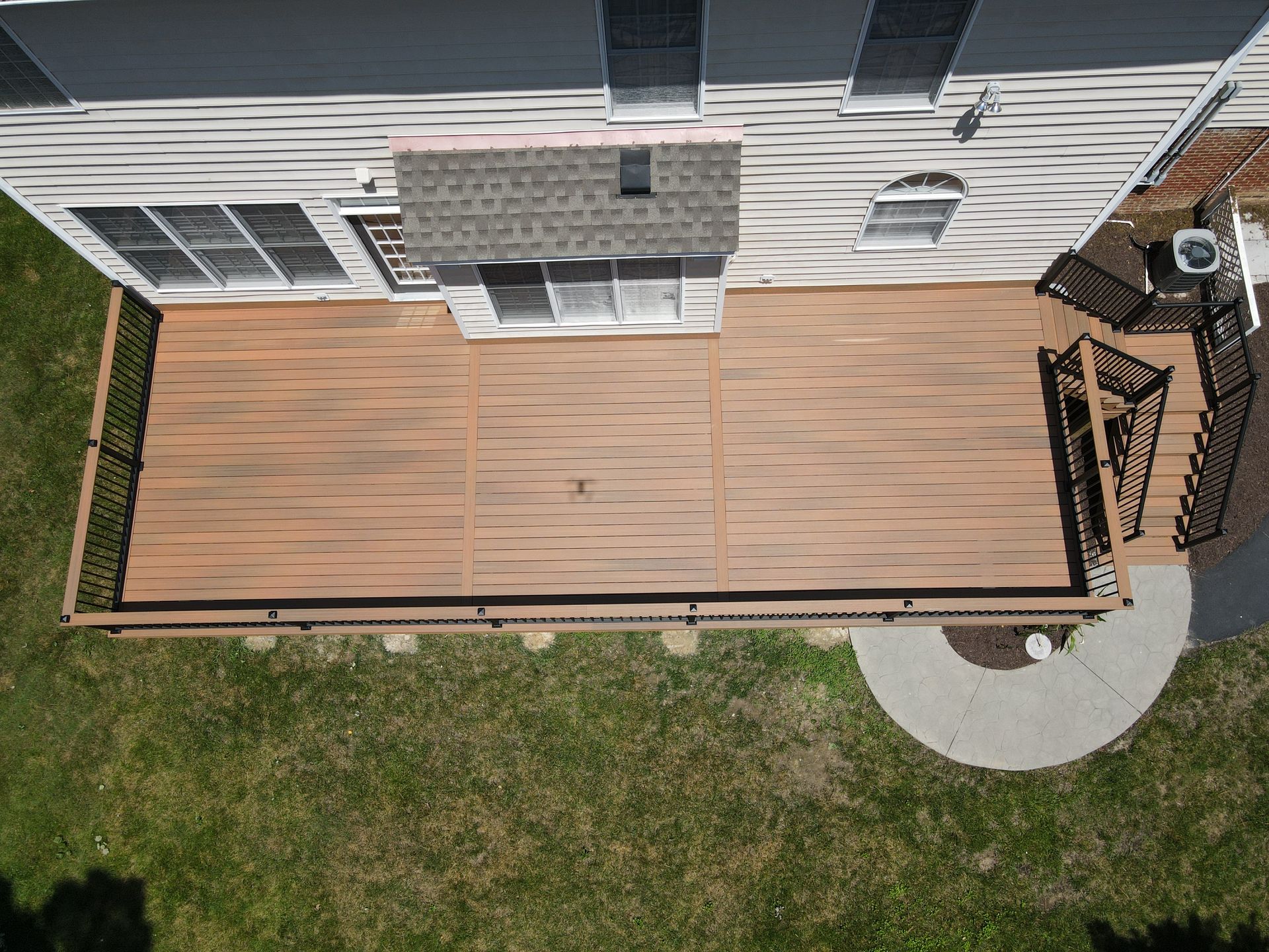 Overhead view of a house deck with wood planks, white siding, stairs, and a small curved patio path
