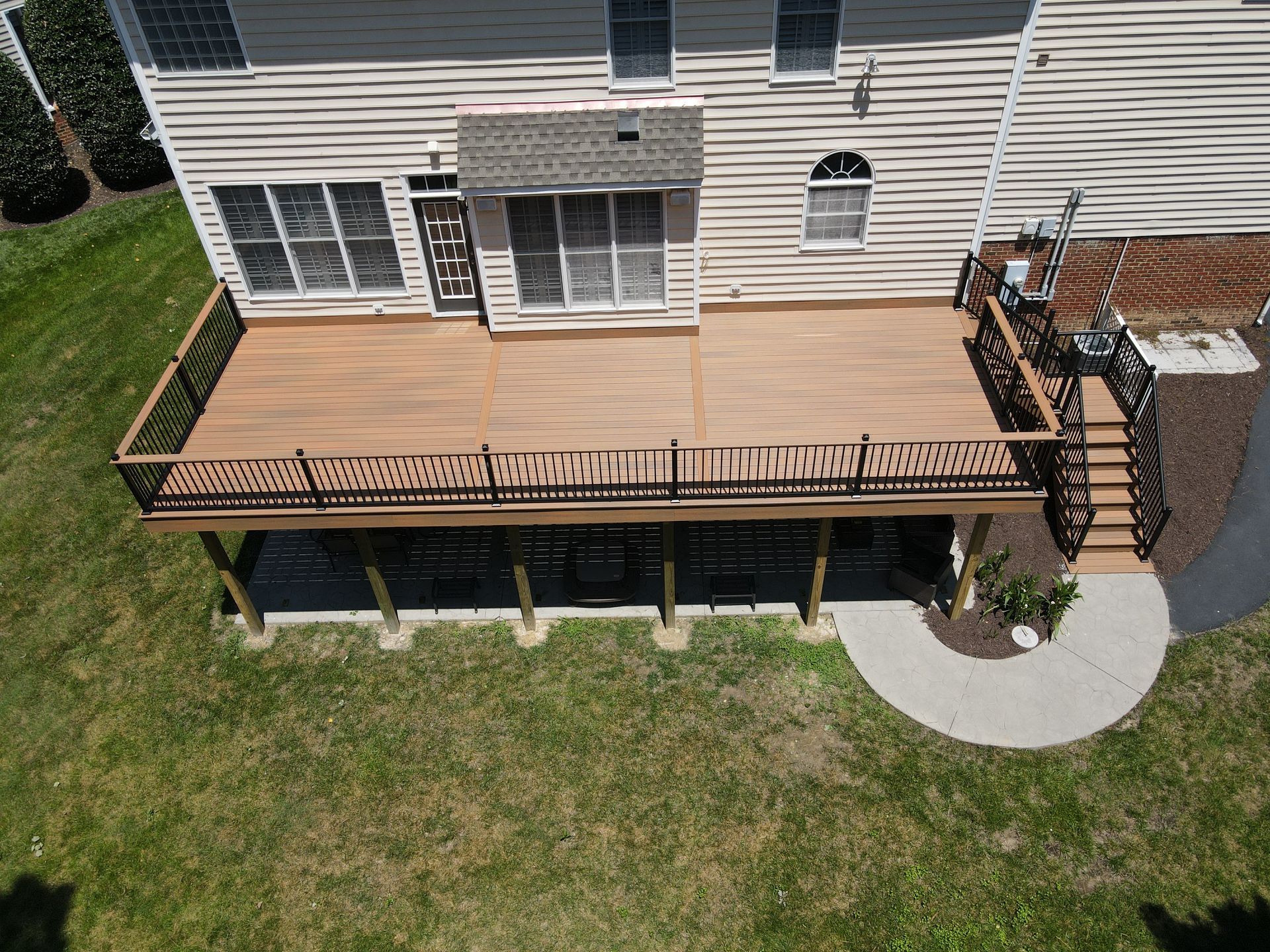 Backyard deck with stairs, railing, and patio furniture beside a house on a grassy lawn