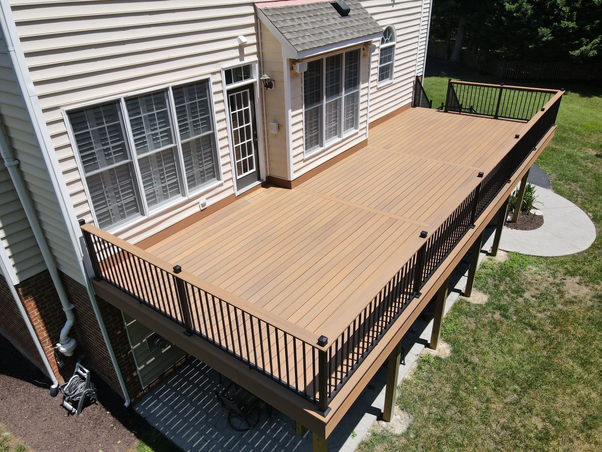 Wooden backyard deck attached to a house, with railing and steps leading to a grassy yard.